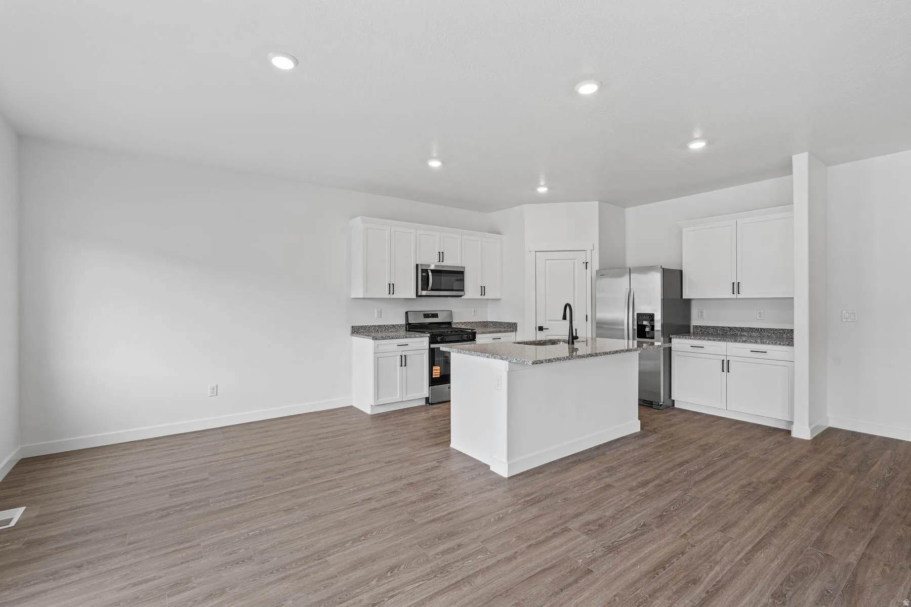 Kitchen featuring stainless steel appliances, white cabinets, a kitchen island with sink, dark stone countertops, and dark wood-style floors