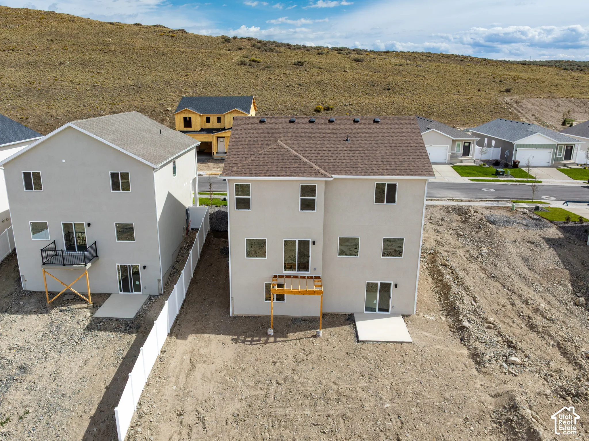 Rear exterior featuring stucco finish, multiple windows, a raised wooden deck, and a ground-level concrete patio
