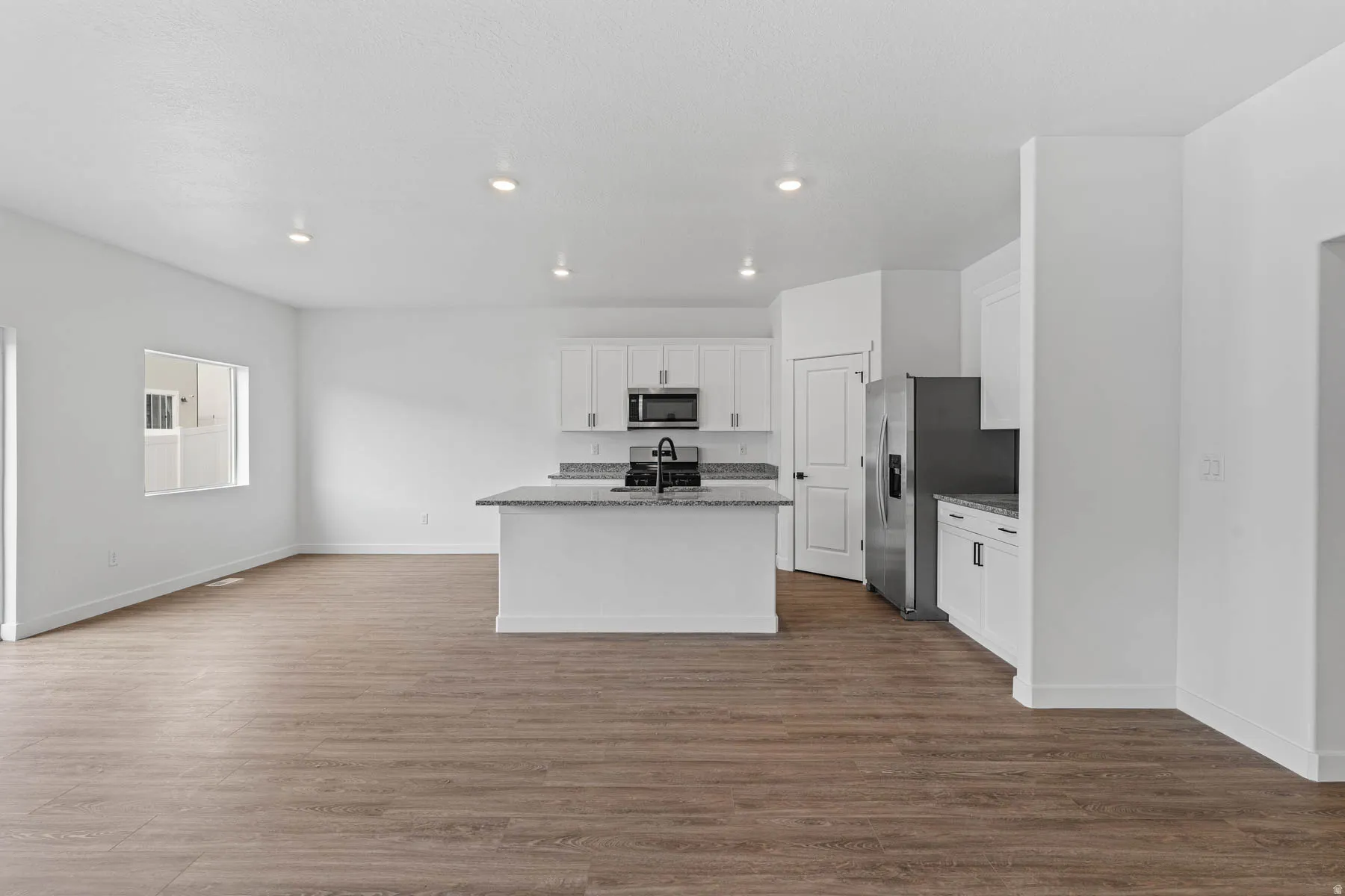 Kitchen with light stone counters, white cabinetry, stainless steel appliances, dark wood finished floors, and an island with sink