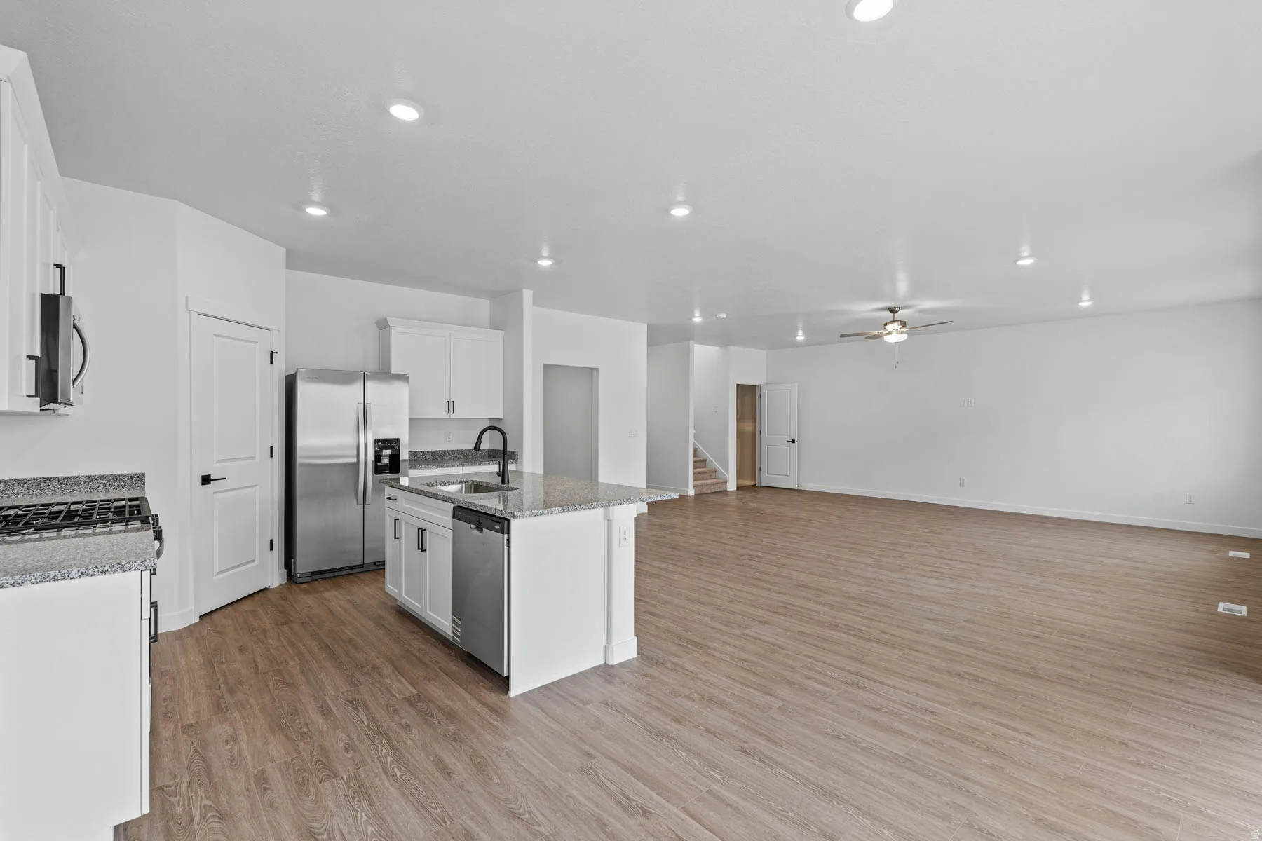 Kitchen with light stone counters, stainless steel appliances, a kitchen island with sink, white cabinetry, and light wood-style flooring