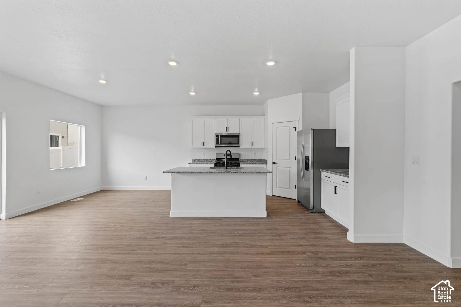 Kitchen with light stone counters, white cabinetry, stainless steel appliances, dark wood finished floors, and an island with sink