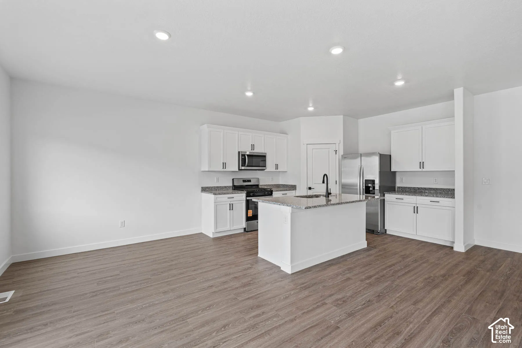 Kitchen featuring stainless steel appliances, white cabinets, a kitchen island with sink, dark stone countertops, and dark wood-style floors