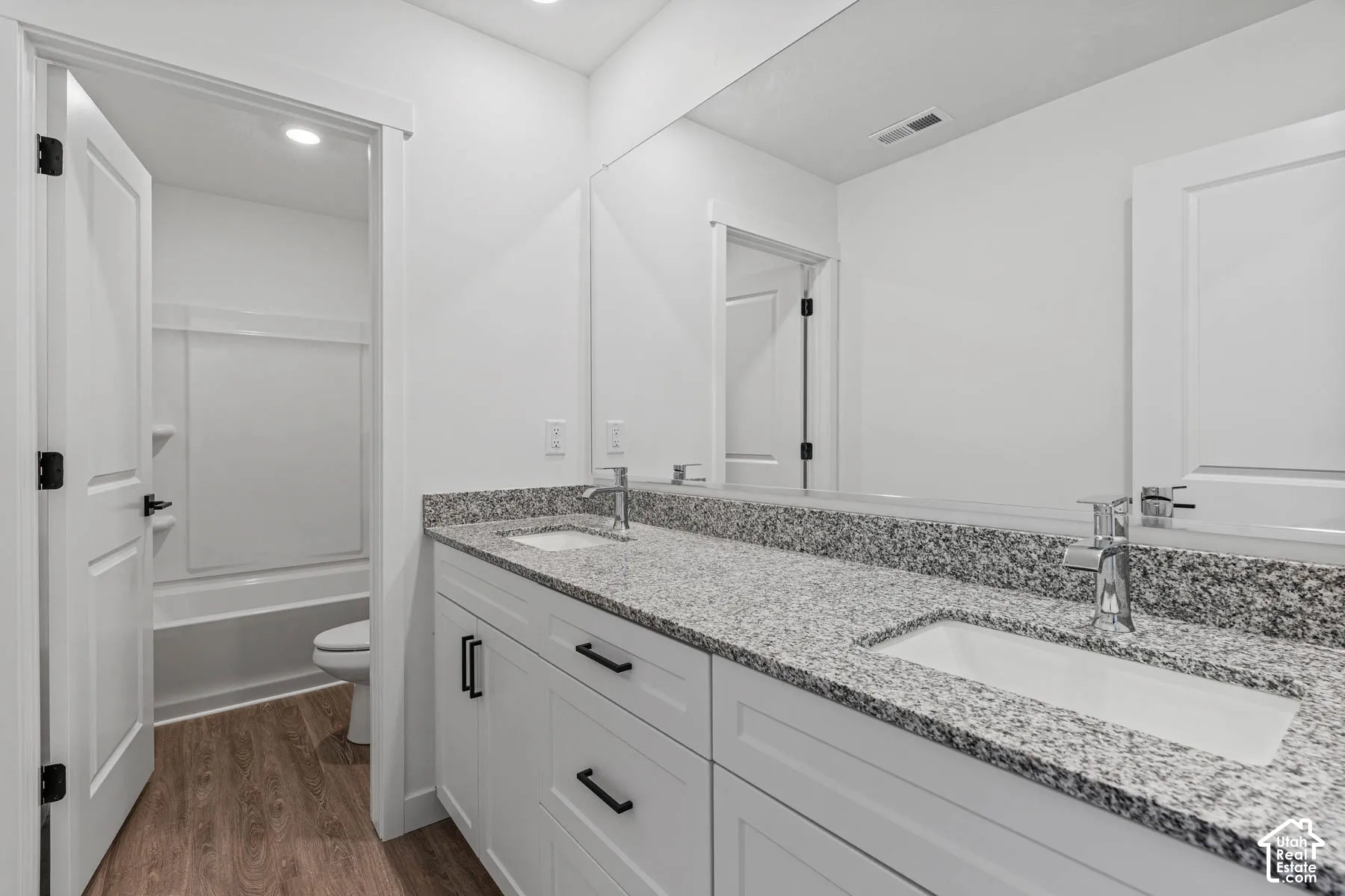 Bathroom with double vanity, dark wood-type flooring, shower / bath combination, and recessed lighting