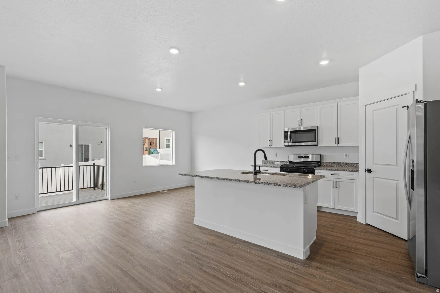 Kitchen with stainless steel appliances, white cabinetry, light stone counters, an island with sink, and recessed lighting
