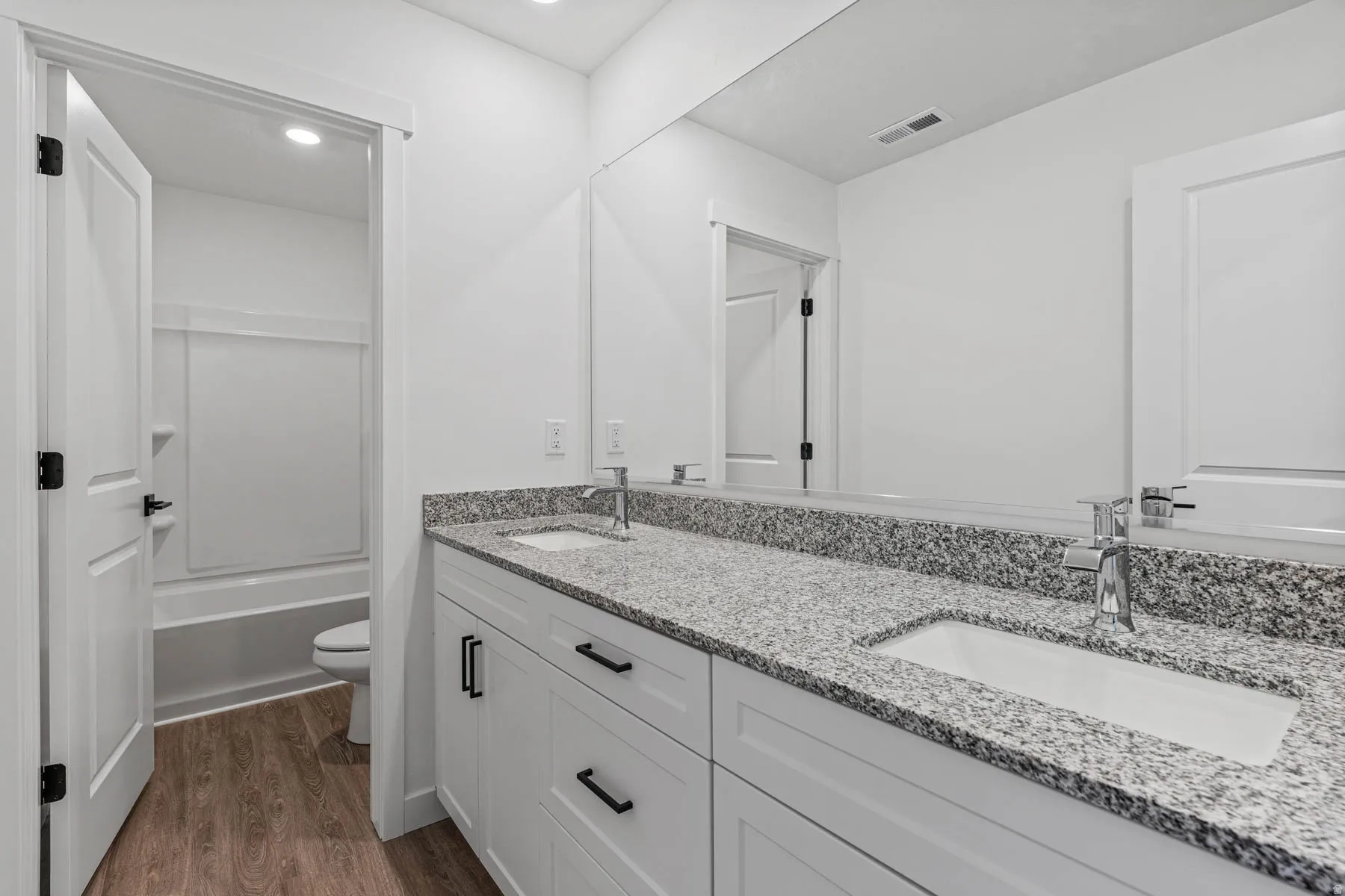 Bathroom with double vanity, dark wood-type flooring, shower / bath combination, and recessed lighting