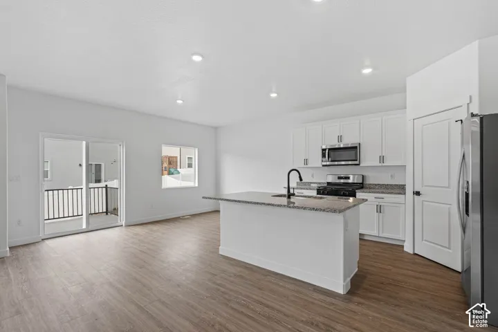 Kitchen with stainless steel appliances, white cabinetry, light stone counters, an island with sink, and recessed lighting