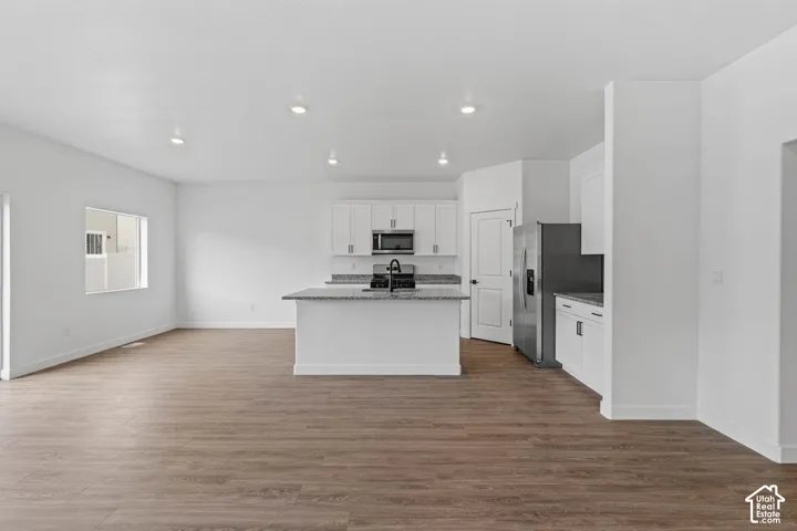 Kitchen with light stone counters, white cabinetry, stainless steel appliances, dark wood finished floors, and an island with sink
