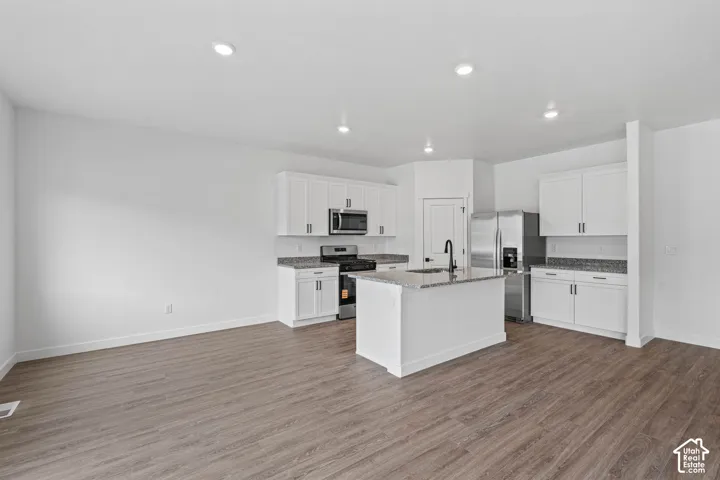 Kitchen featuring stainless steel appliances, white cabinets, a kitchen island with sink, dark stone countertops, and dark wood-style floors