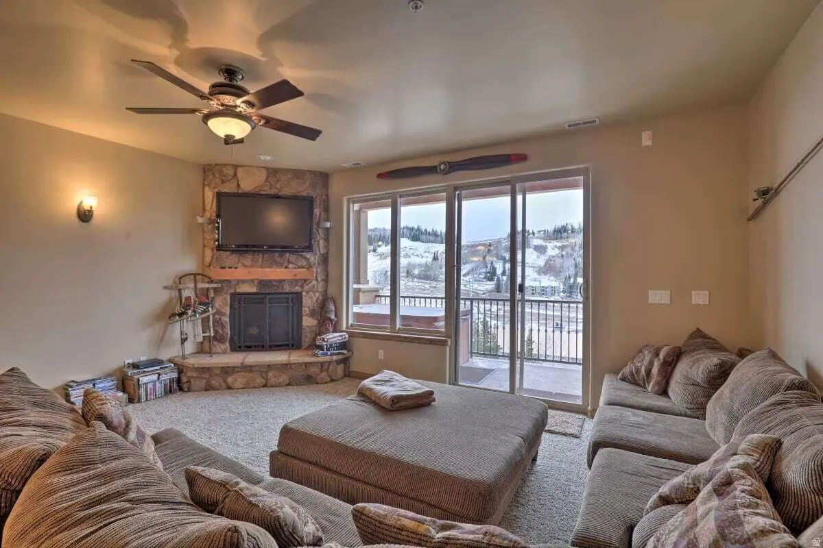 Living area with a stone fireplace, ceiling fan, and carpet flooring