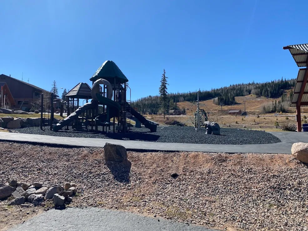 Community playground featuring a multi-level play structure with slides, a climbing net, and a covered gazebo