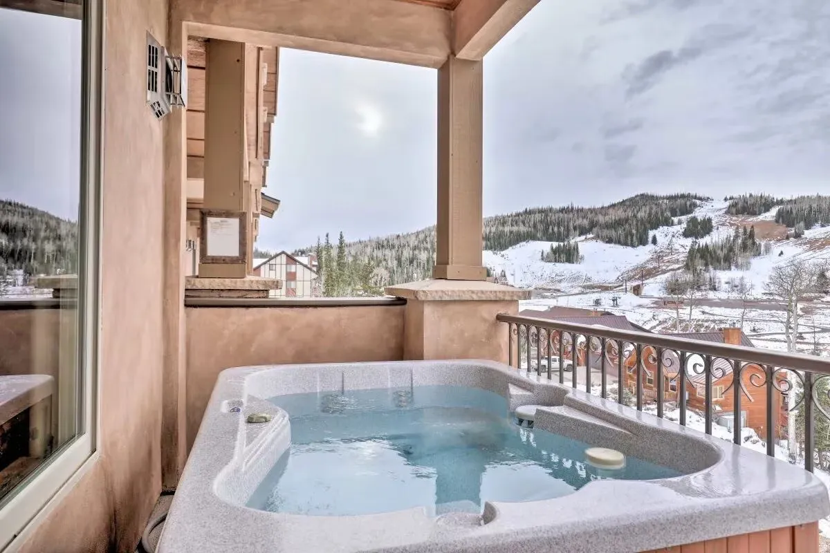 Snow covered back of property featuring a mountain view and a hot tub