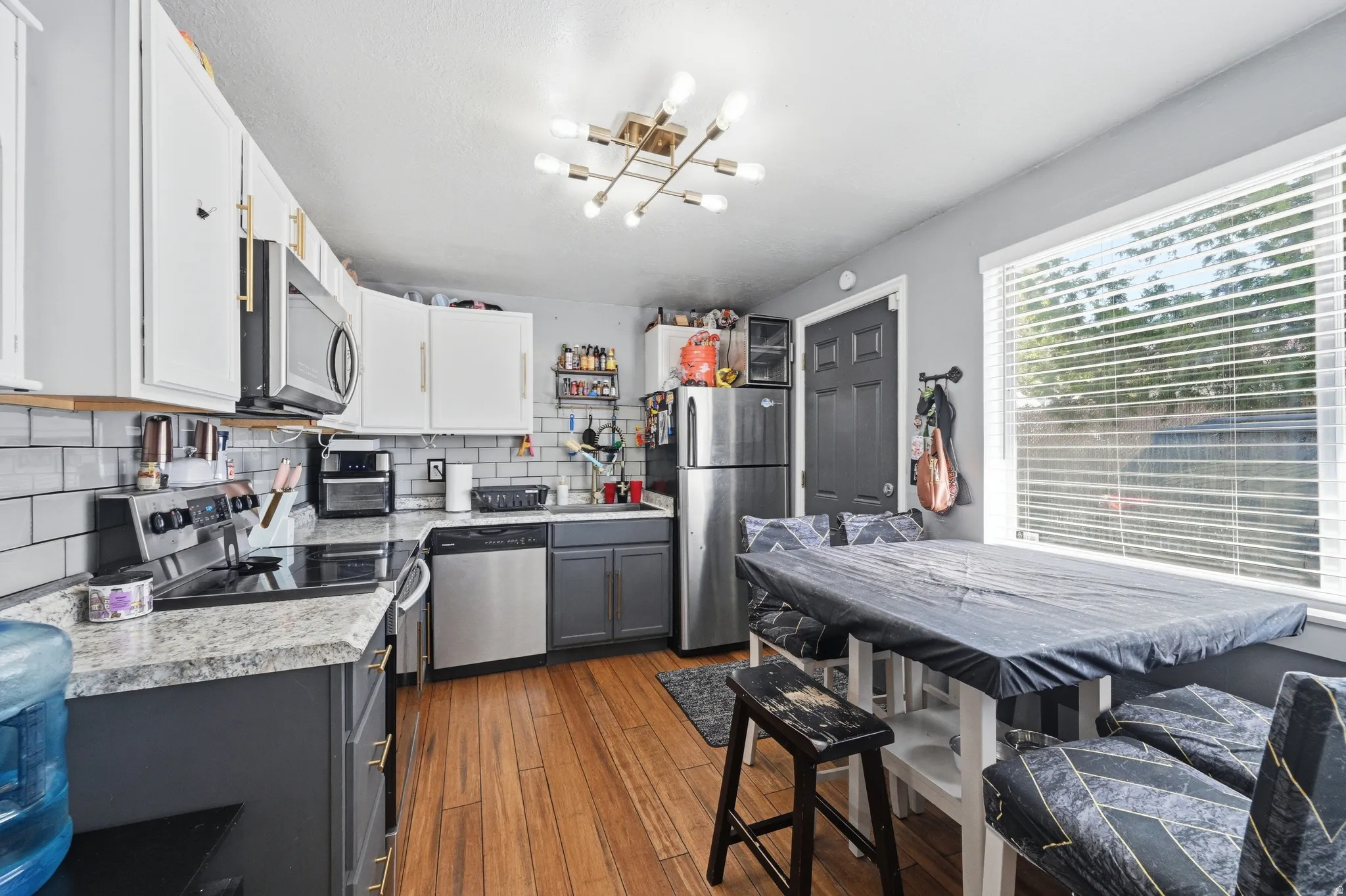 Two tone kitchen featuring two tone color scheme, light countertops, stainless steel appliances, light wood finished floors, and decorative backsplash