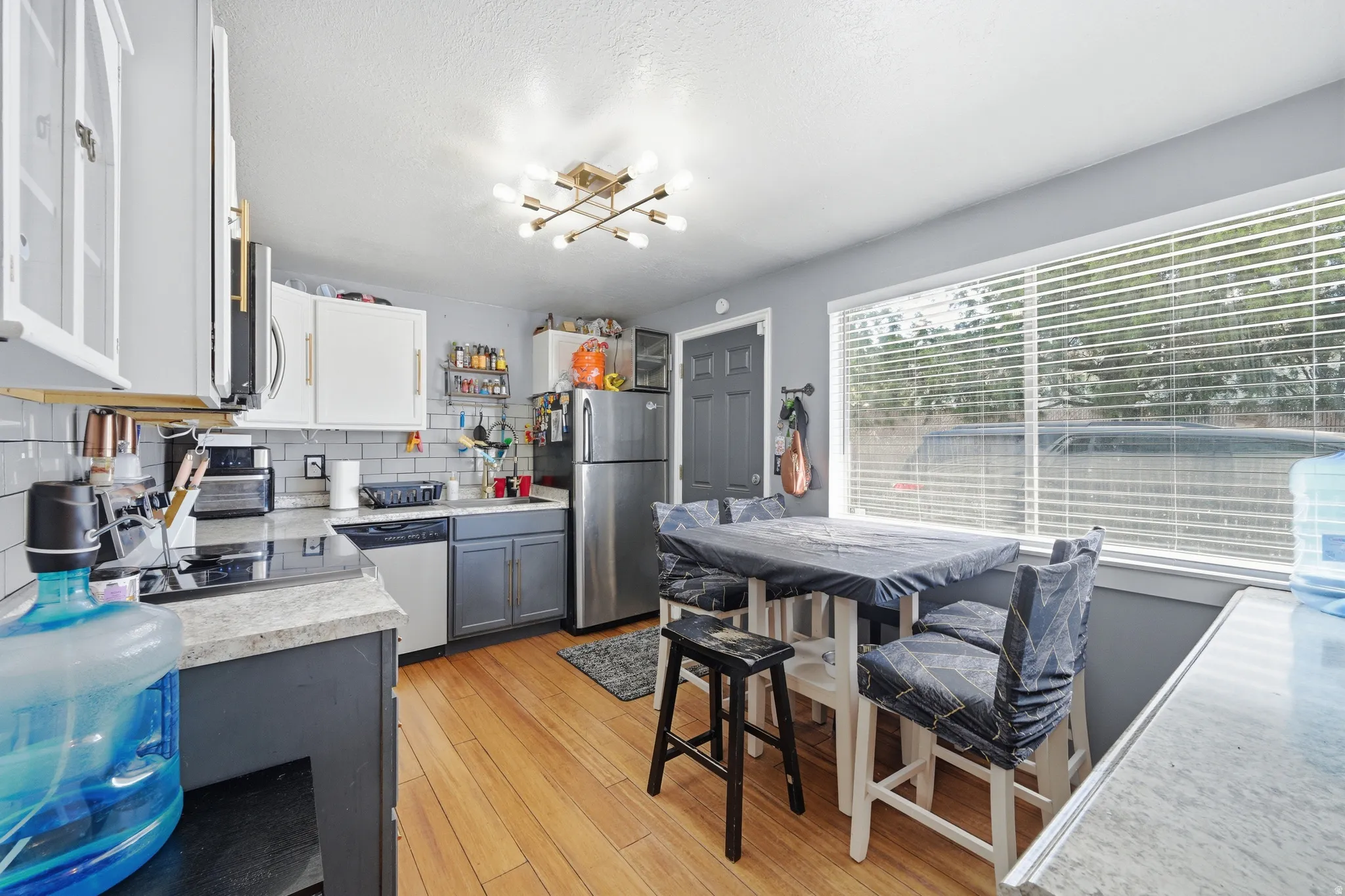 Kitchen with light countertops, stainless steel appliances, backsplash, two tone cabinets, and light wood finished floors