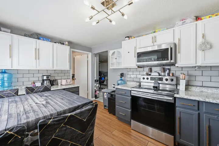 Two tone kitchen with dual tone cabinets, stainless steel appliances, decorative backsplash, and light stone counters