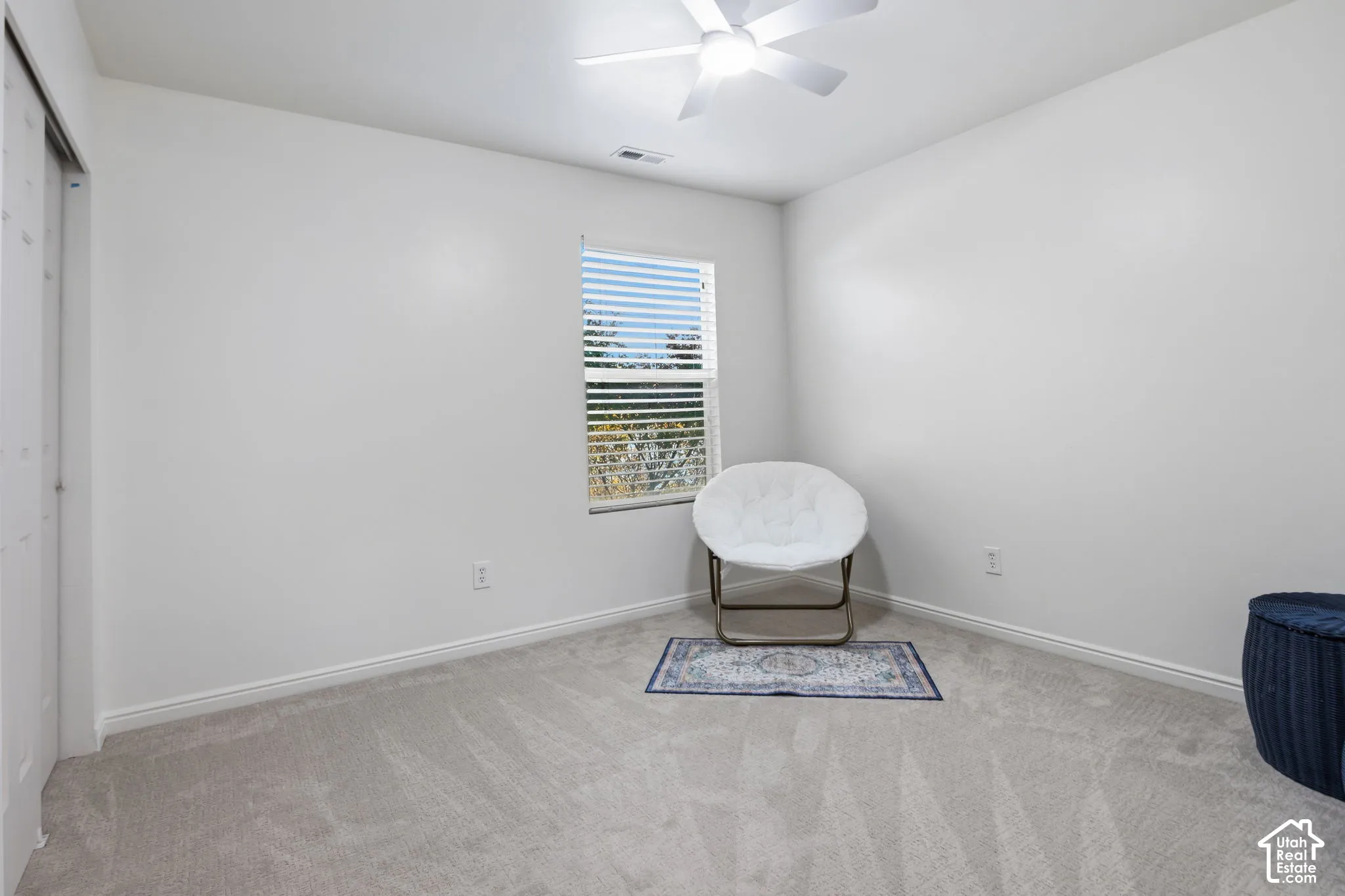 Carpeted flooring with white baseboards, a single window with blinds, and an overhead ceiling fan