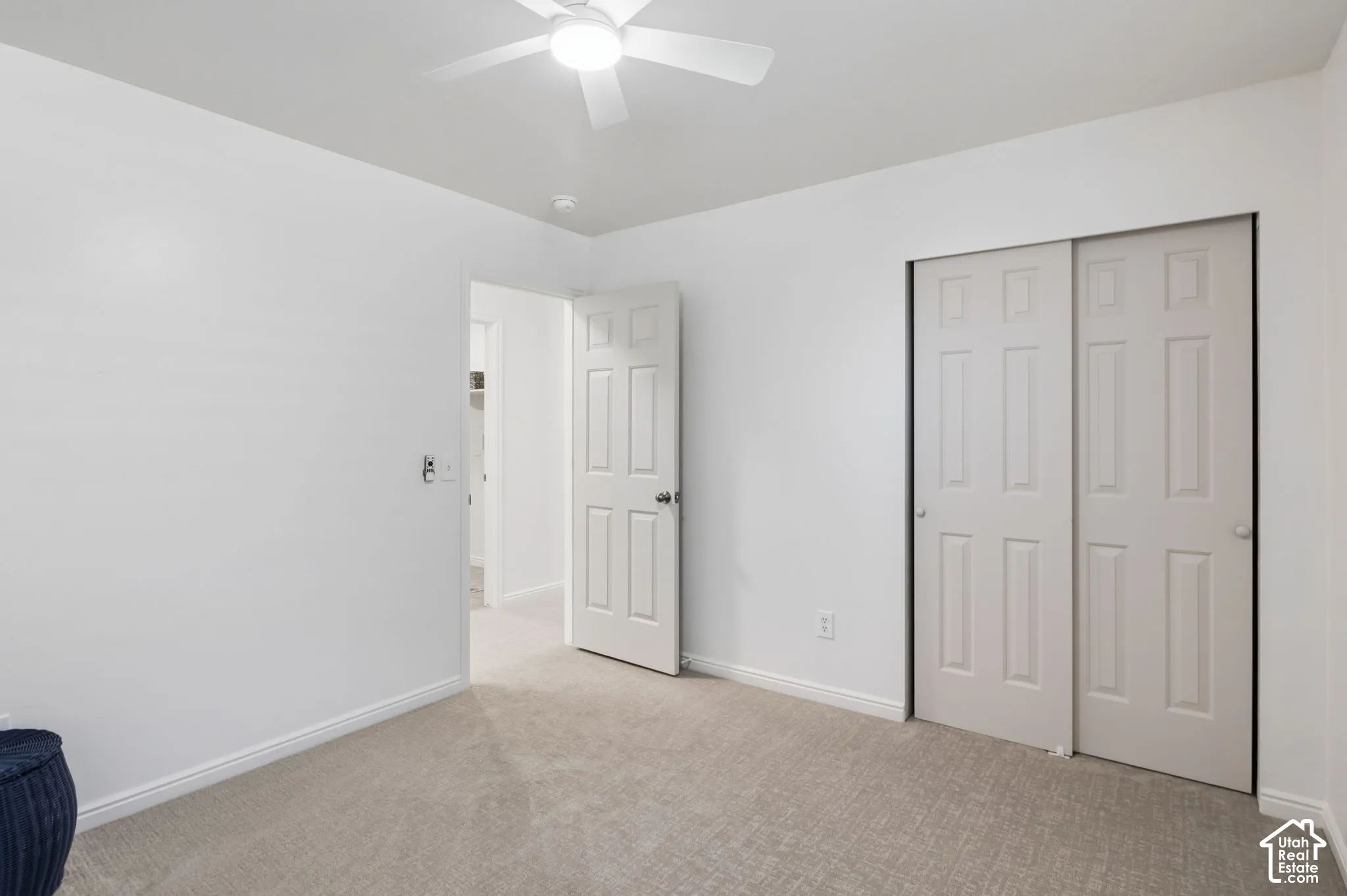 Neutral tone wall paint, carpeted flooring, a ceiling fan with integrated lighting, and a closet with sliding panel doors