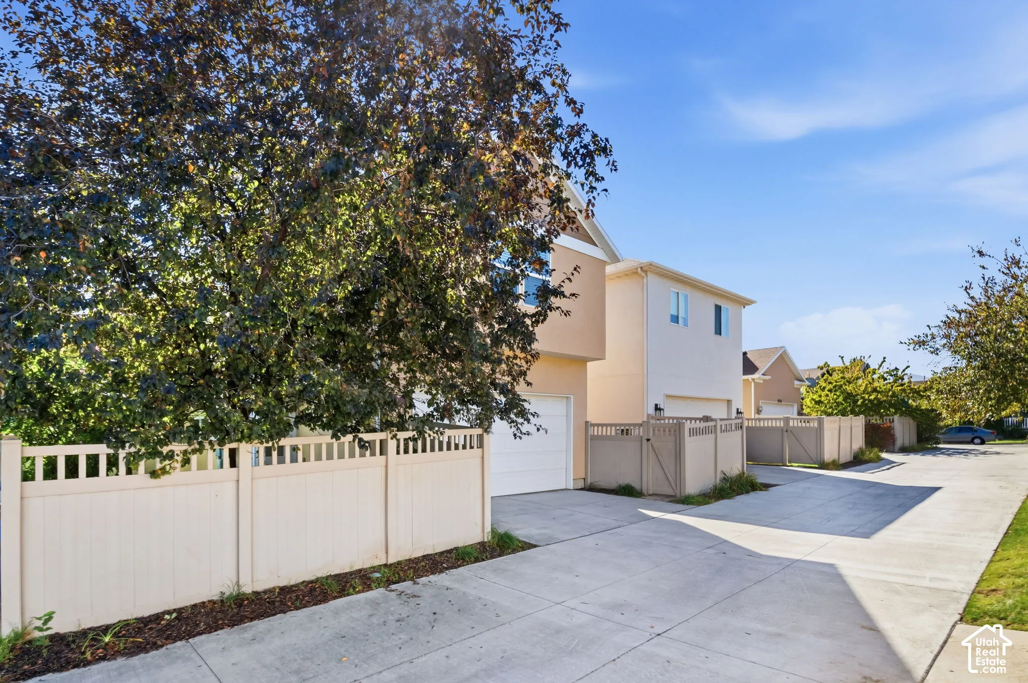 Multi-level exterior with a light stucco finish, featuring a prominent garage door and a neutral-toned privacy fence