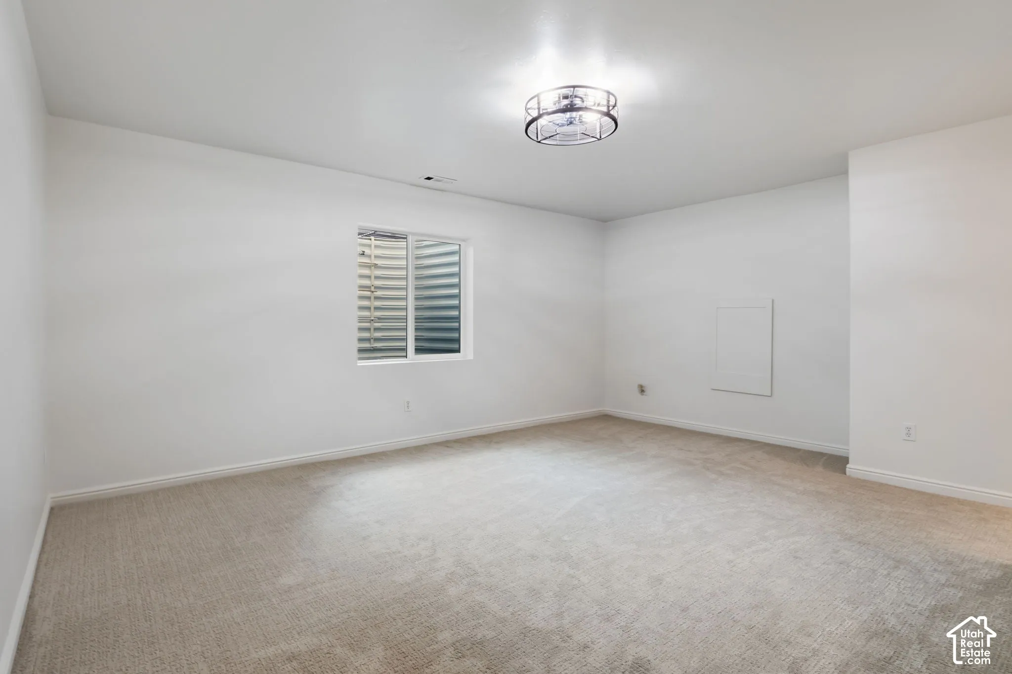 Recessed window with white trim, light-colored carpet flooring, white walls, and a ceiling-mounted light fixture