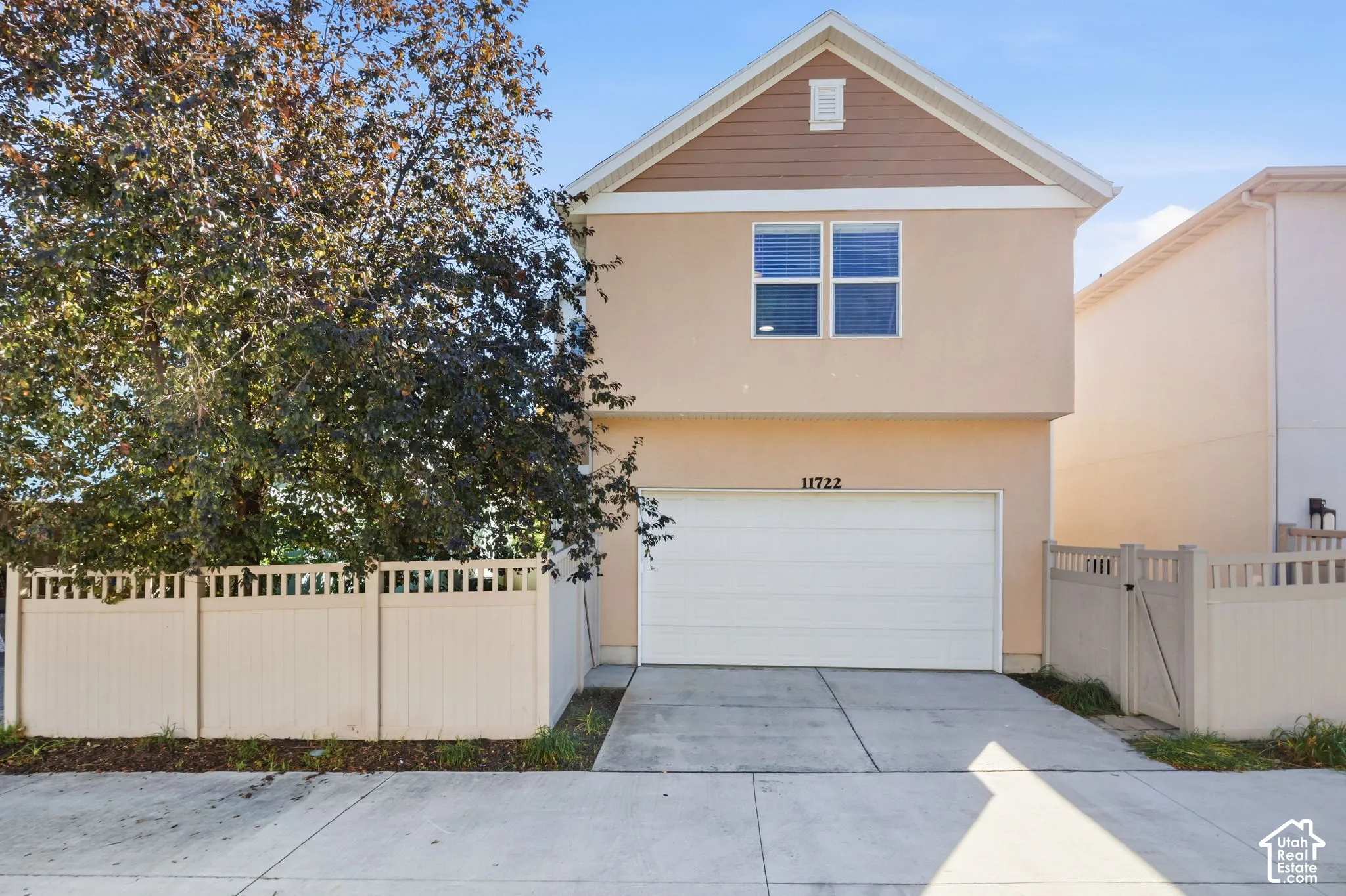 Stucco exterior with a peaked roofline, an attached two-car garage, a paved driveway, and a privacy fence