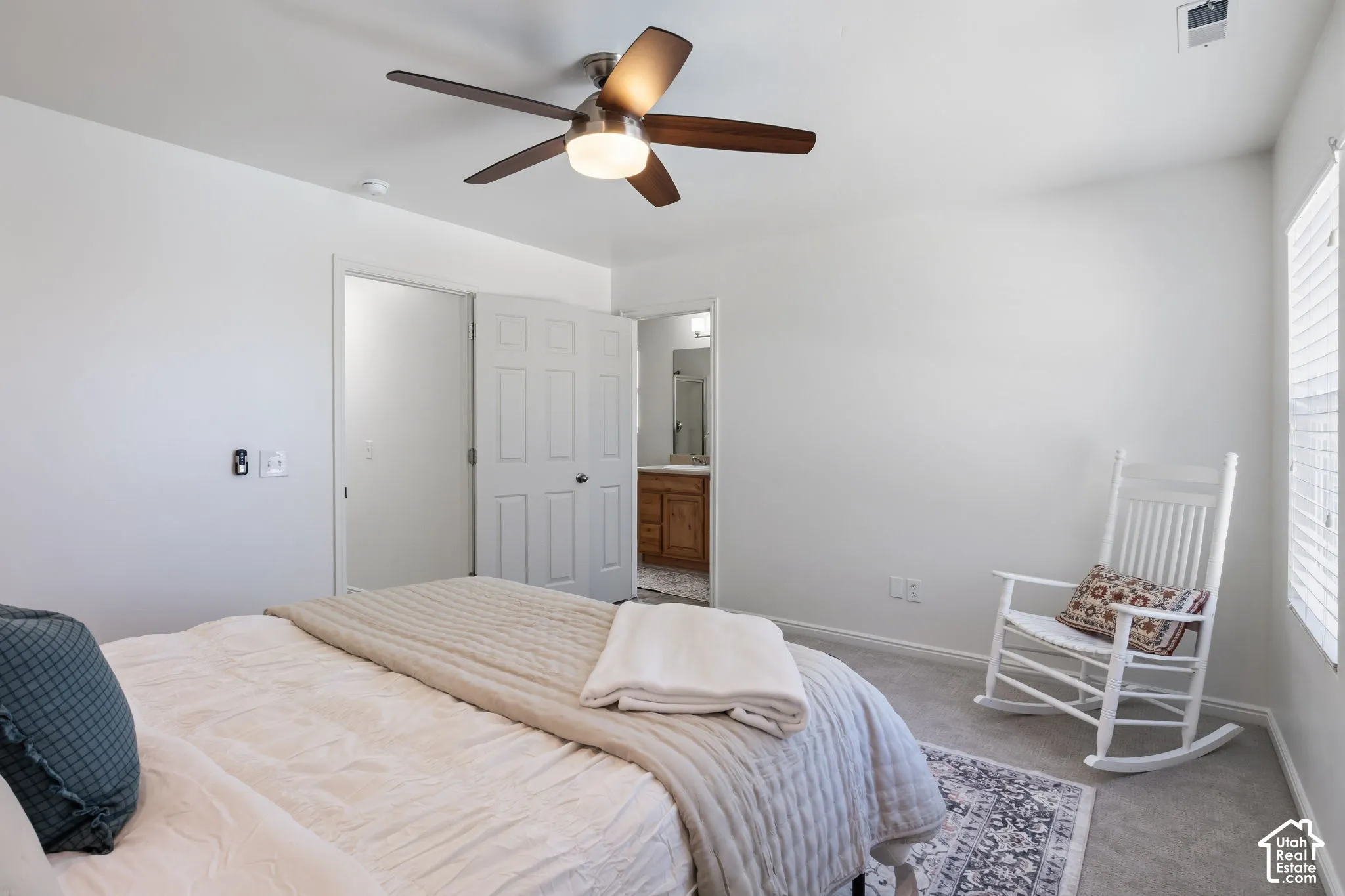 Carpeted bedroom with a ceiling fan, white paneled door, and window with blinds