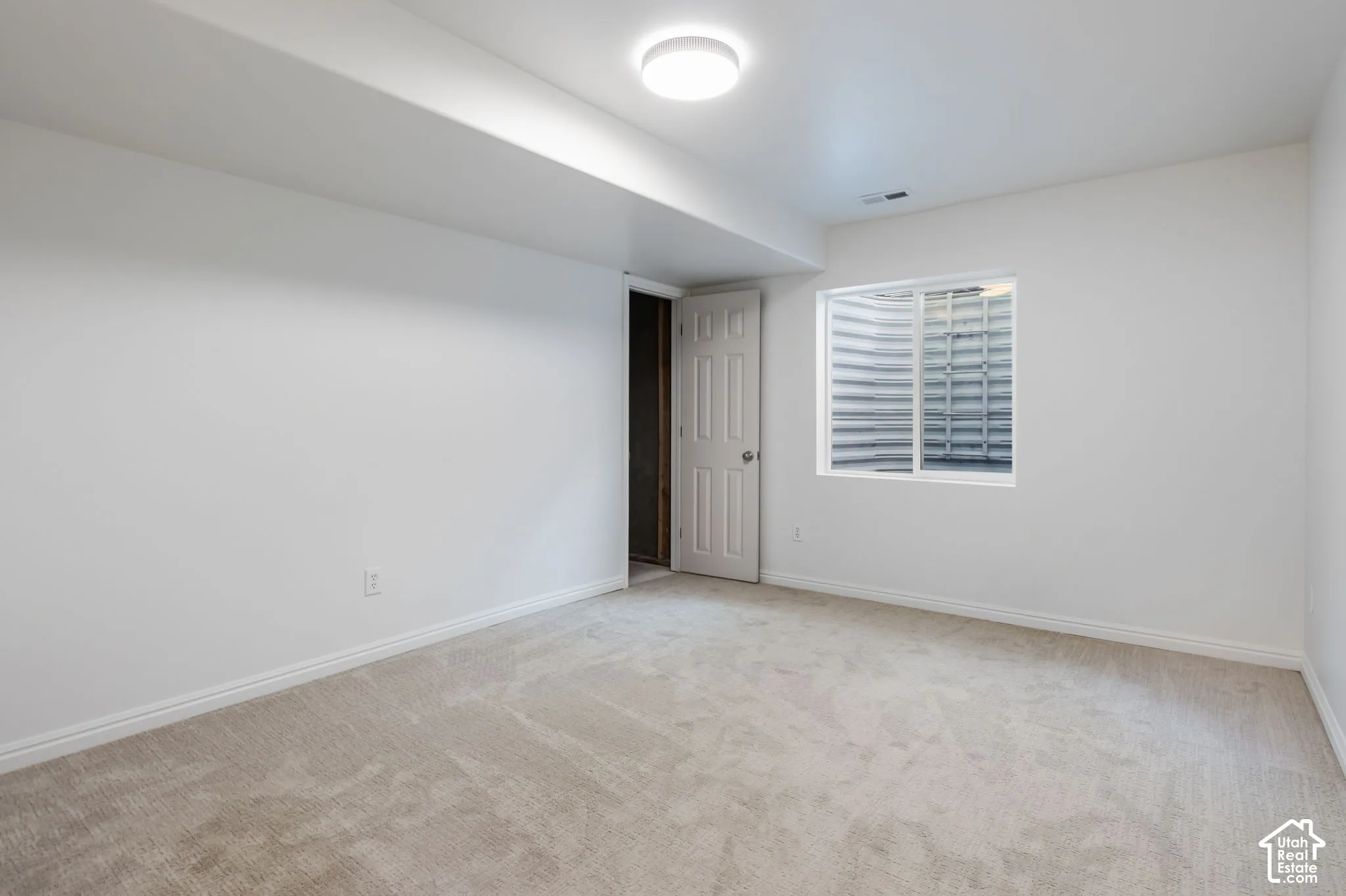 Light-toned carpeting, white walls, and a window with a well-cover