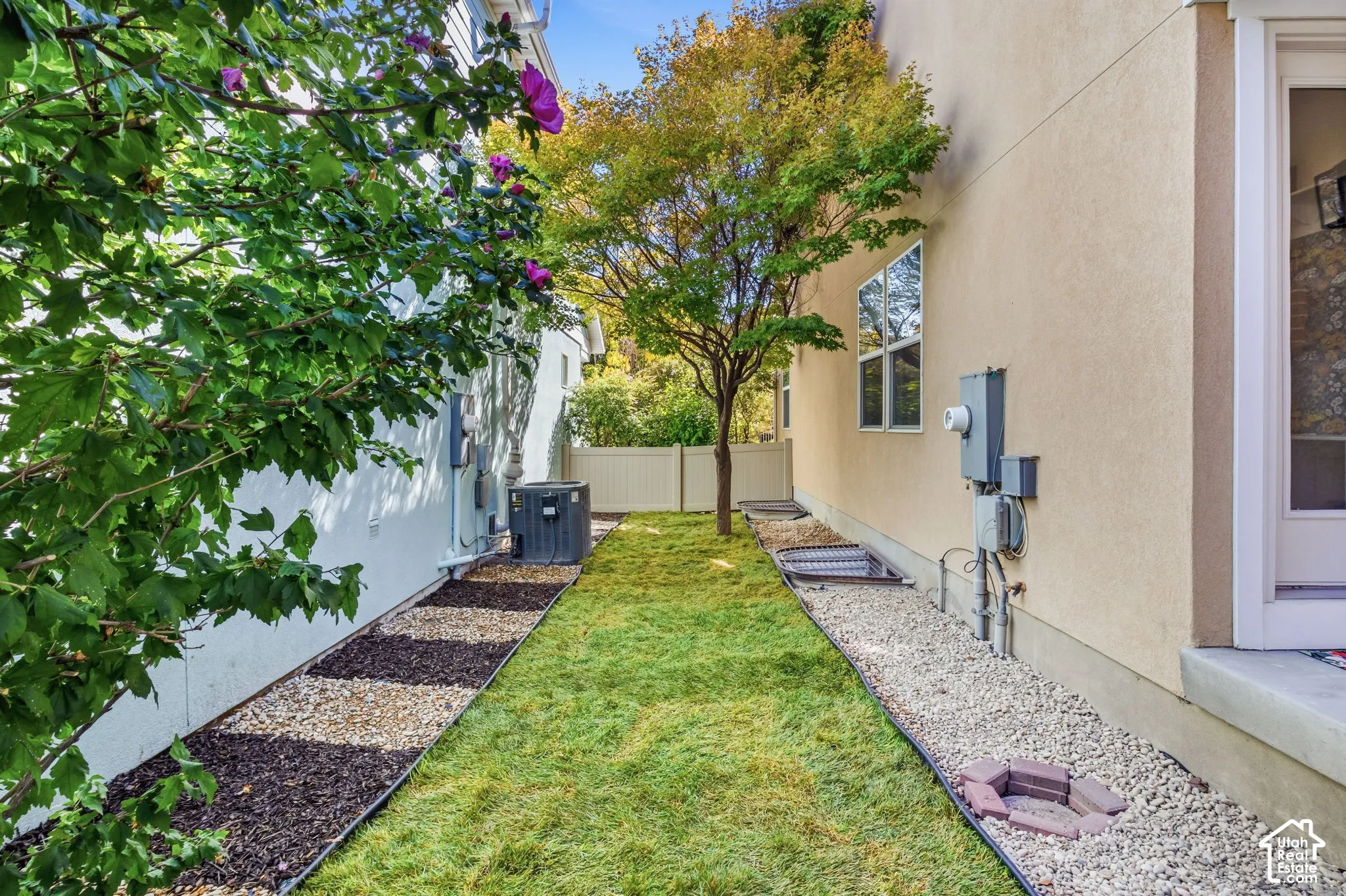 Manicured lawn with gravel and dark mulch borders, mature trees, and a privacy fence
