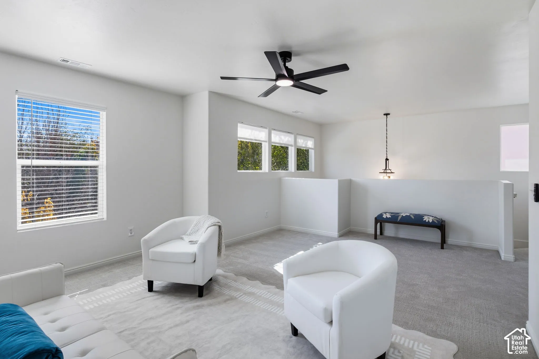 Loft area featuring carpeted flooring, multiple windows with blinds, a black ceiling fan, and a contemporary pendant light fixture
