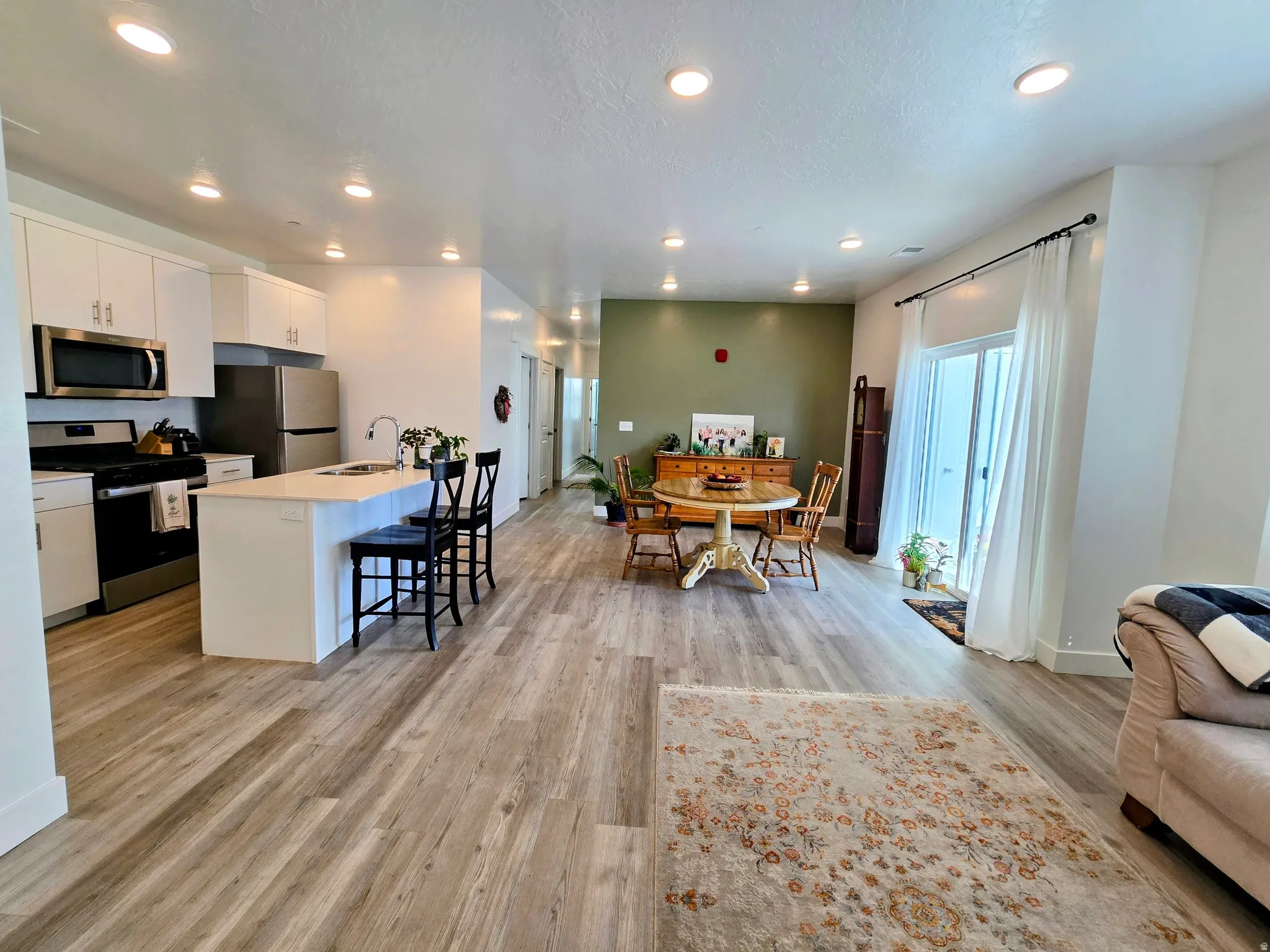 Kitchen with open floor plan, a center island with sink, white cabinets, stainless steel appliances, and a breakfast bar area