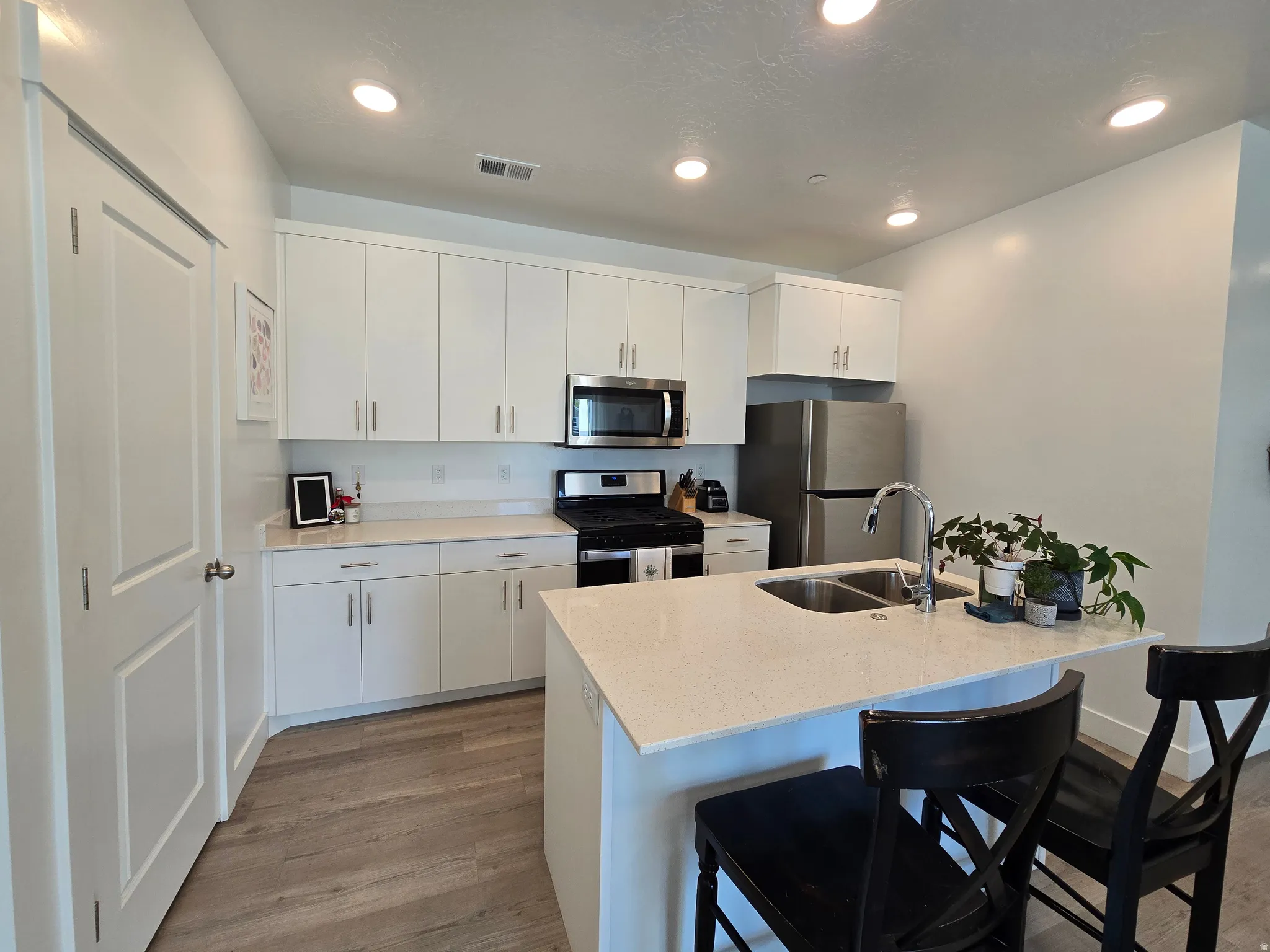Kitchen featuring stainless steel appliances, a kitchen breakfast bar, dark wood-type flooring, light stone countertops, and recessed lighting