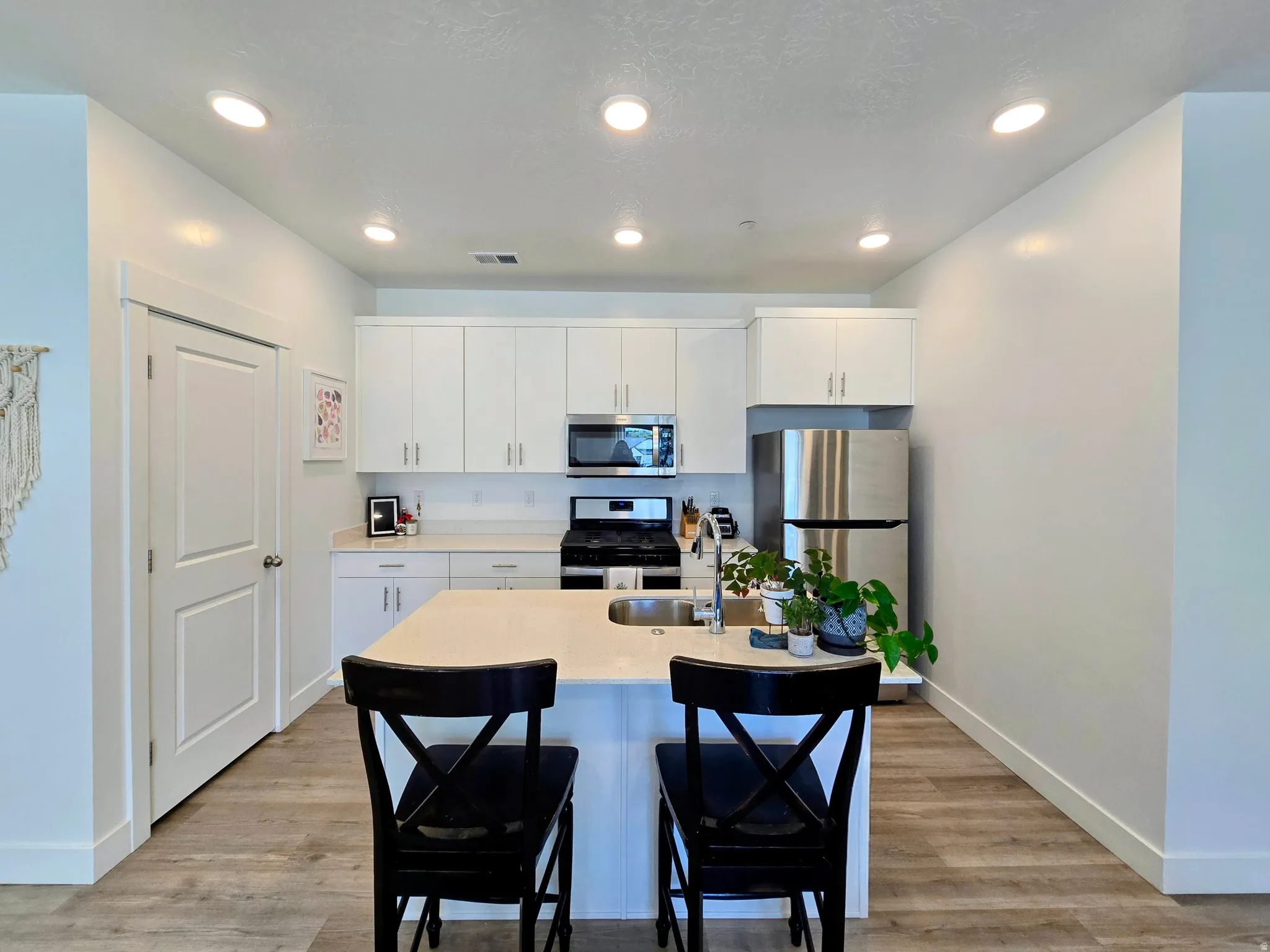 Kitchen featuring stainless steel appliances, light wood-type flooring, a breakfast bar, white cabinets, and recessed lighting