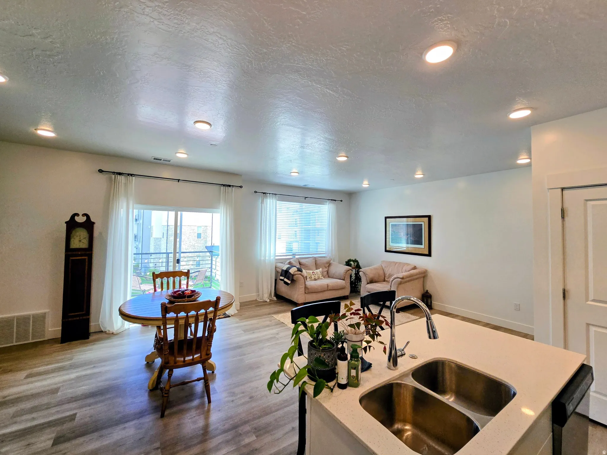 Kitchen with a textured ceiling, wood finished floors, open floor plan, light stone countertops, and recessed lighting
