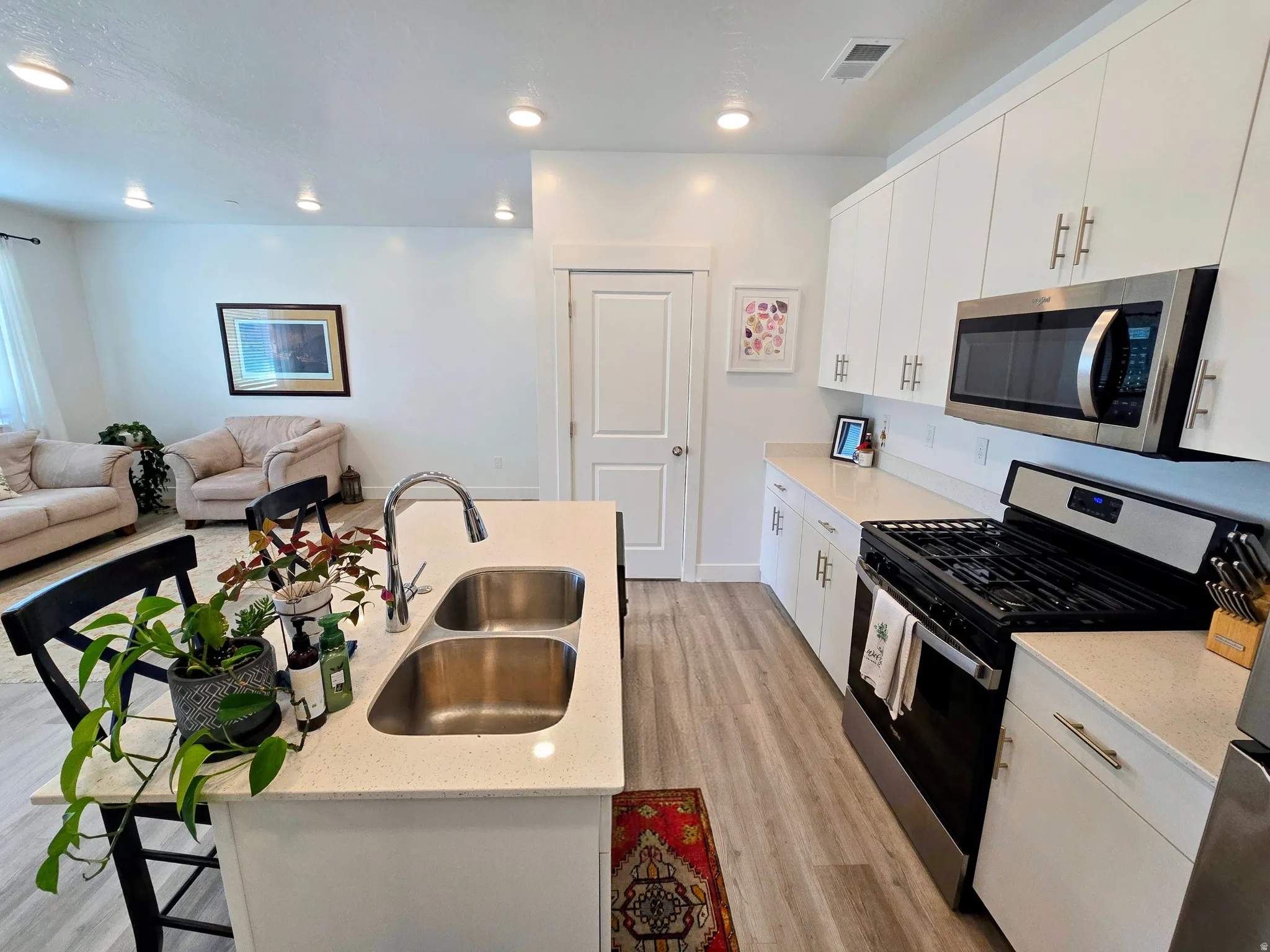 Kitchen featuring stainless steel appliances, white cabinetry, a kitchen island with sink, open floor plan, and a breakfast bar