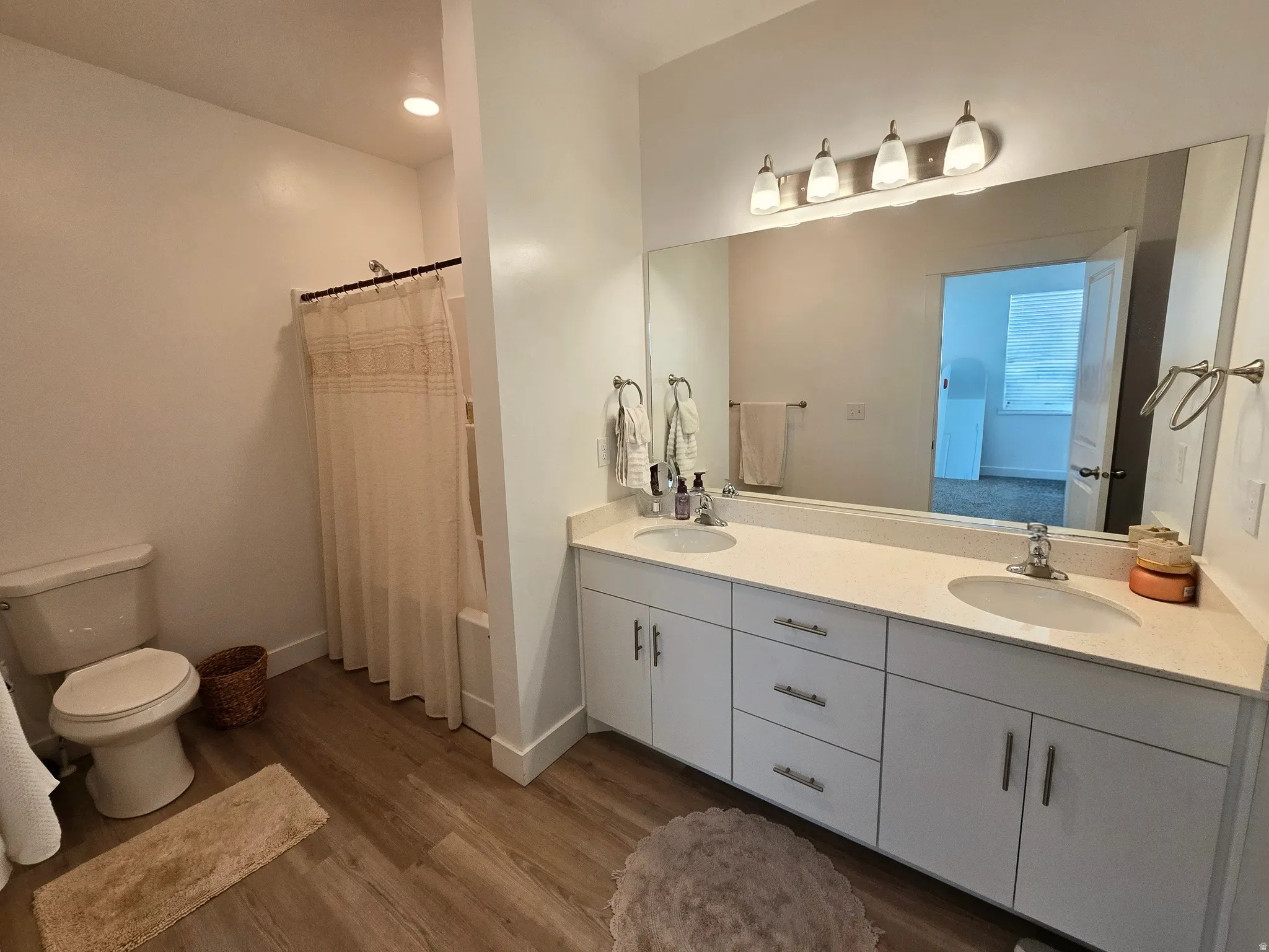 Bathroom featuring double vanity, curtained shower, and dark wood-style flooring