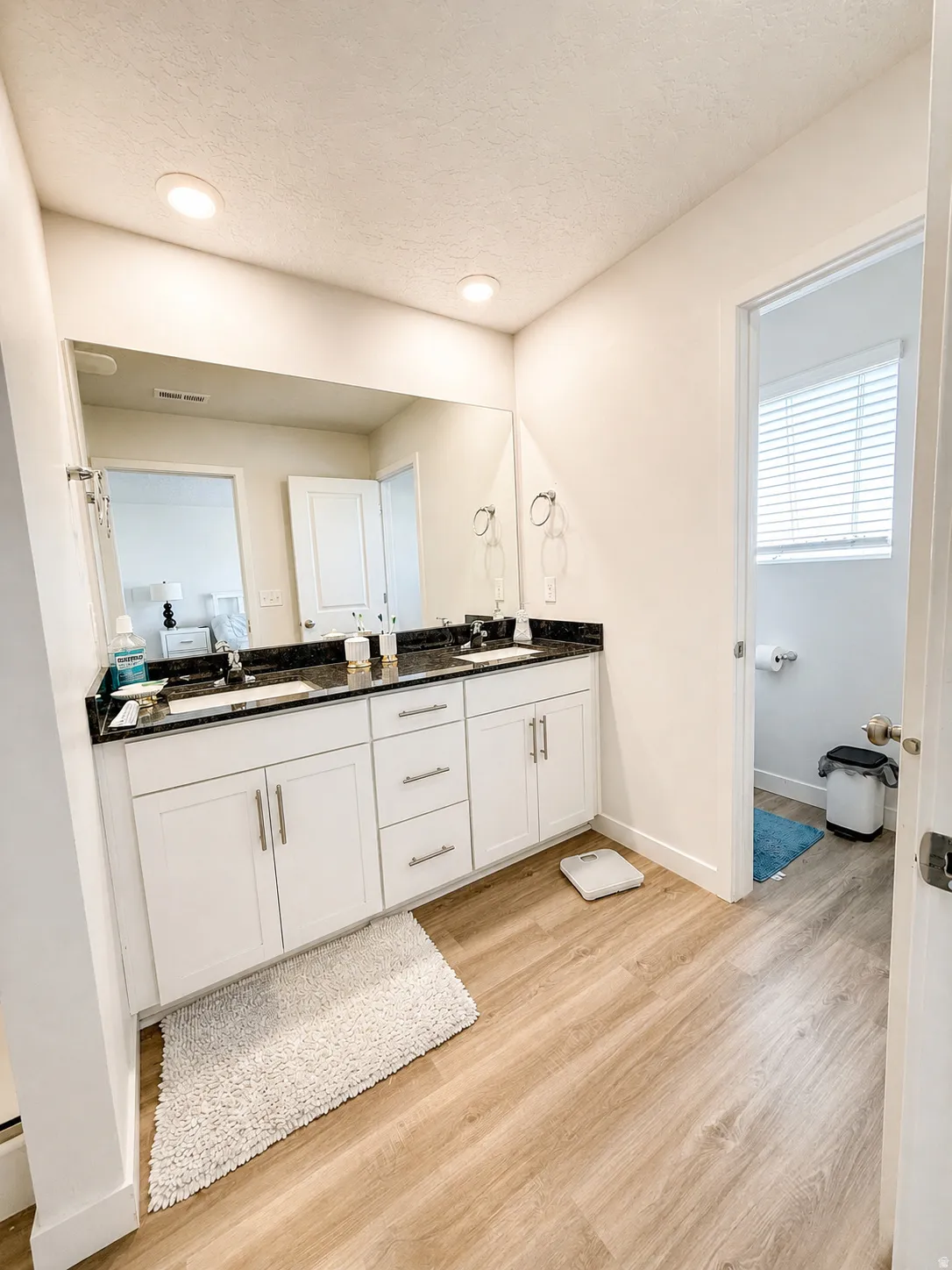 Full bathroom with double vanity, light wood-style flooring, a textured ceiling, and recessed lighting