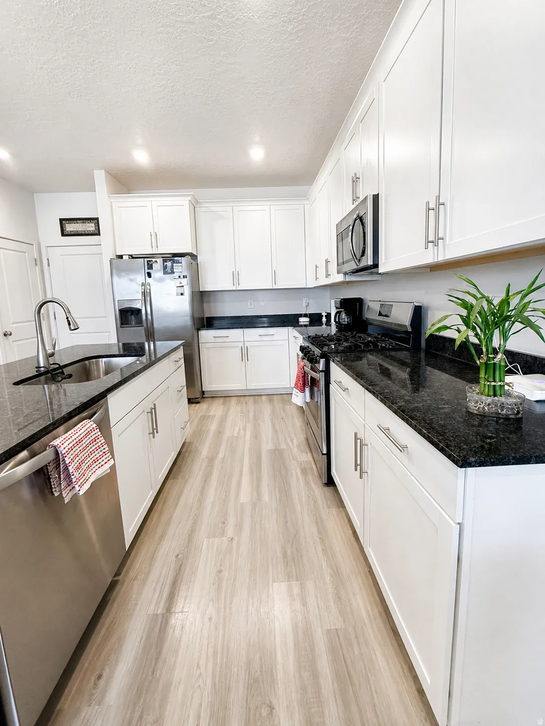 Kitchen featuring stainless steel appliances, dark stone countertops, light wood finished floors, white cabinets, and a textured ceiling