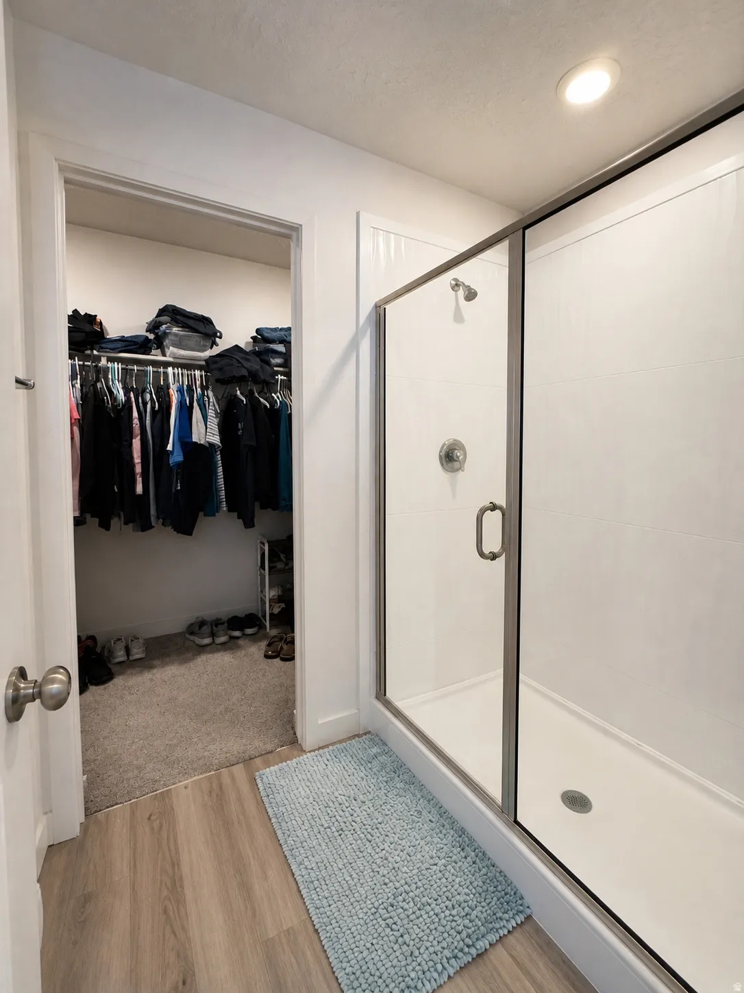 Full bath featuring a spacious closet, light wood finished floors, a shower stall, and a textured ceiling