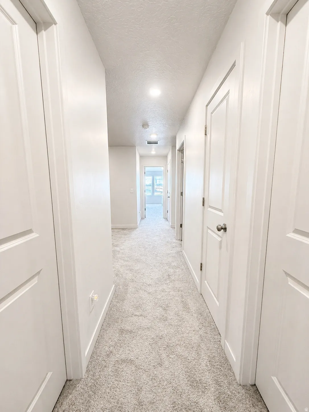 Hallway featuring light carpet and a textured ceiling