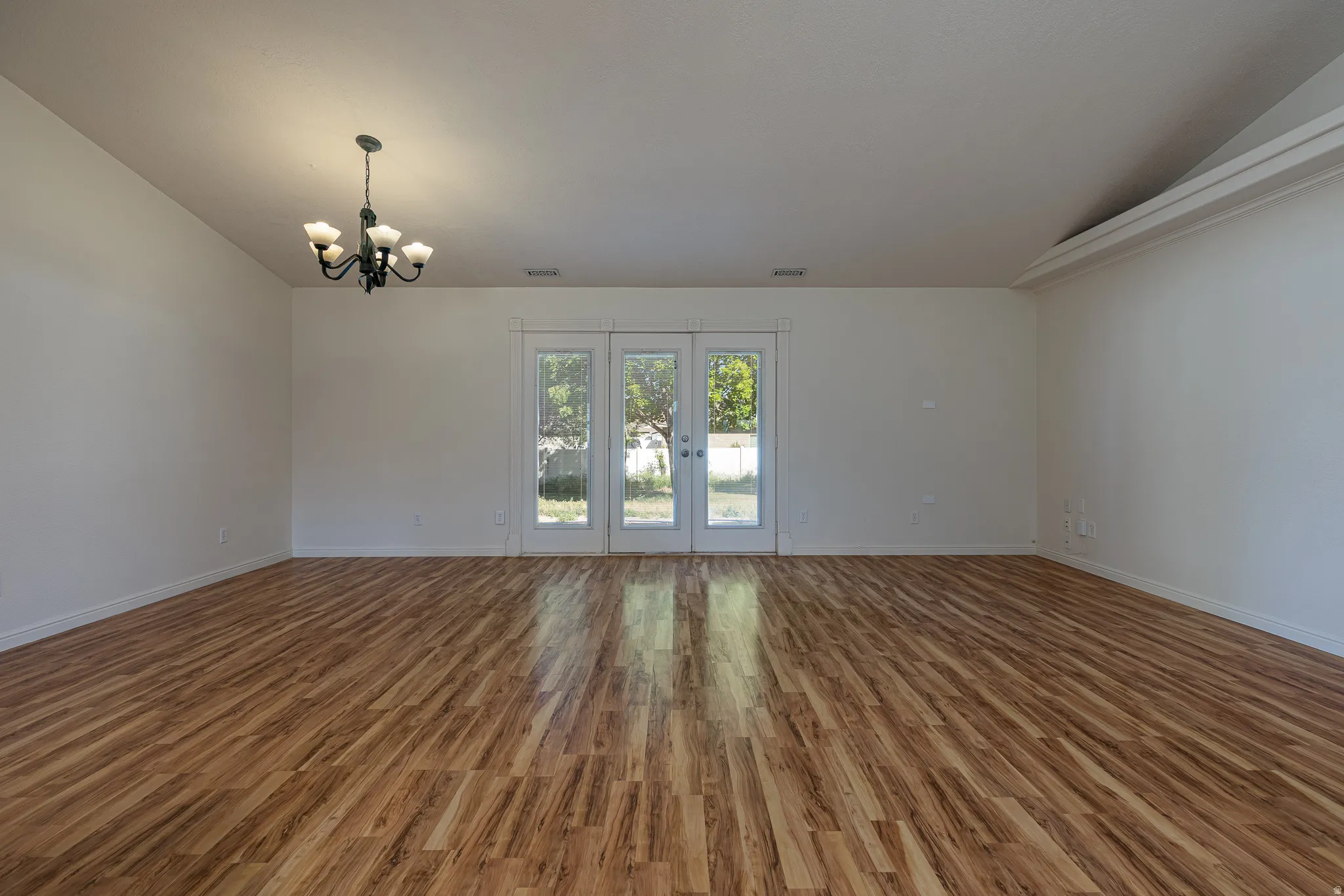 Empty room with lofted ceiling, wood finished floors, a chandelier, and french doors
