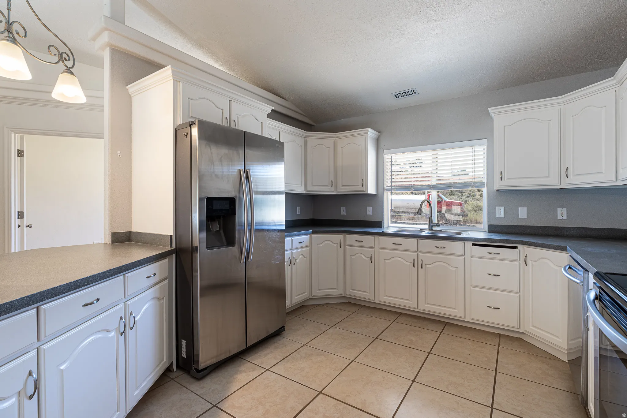 Kitchen featuring stainless steel appliances, white cabinetry, dark countertops, and light tile patterned flooring