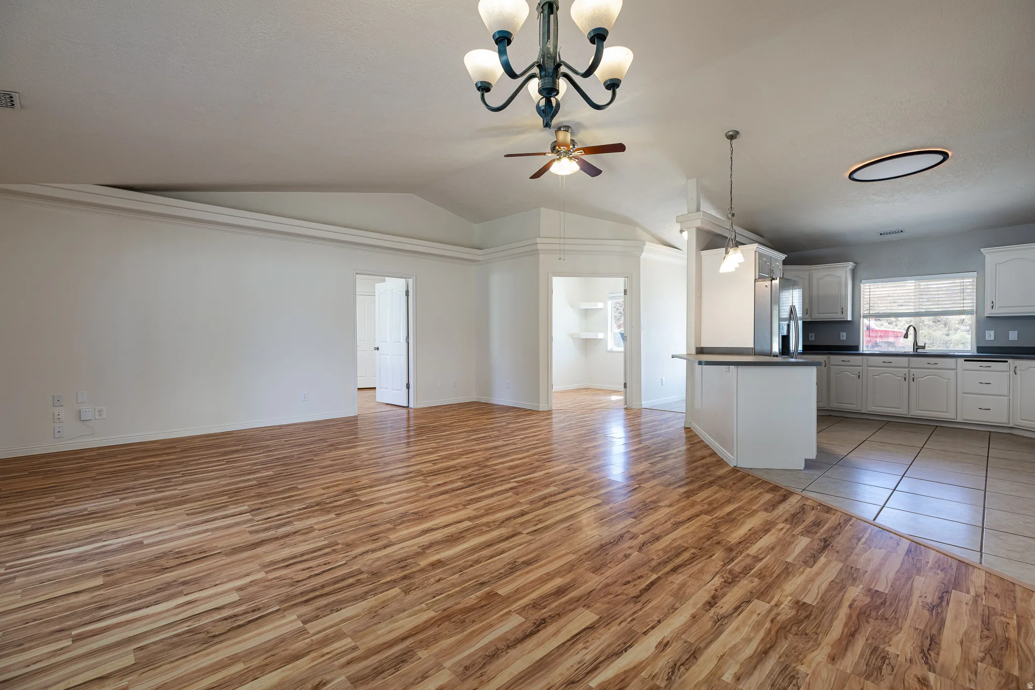 Kitchen featuring dark countertops, open floor plan, hanging lights, white cabinets, and stainless steel fridge with ice dispenser