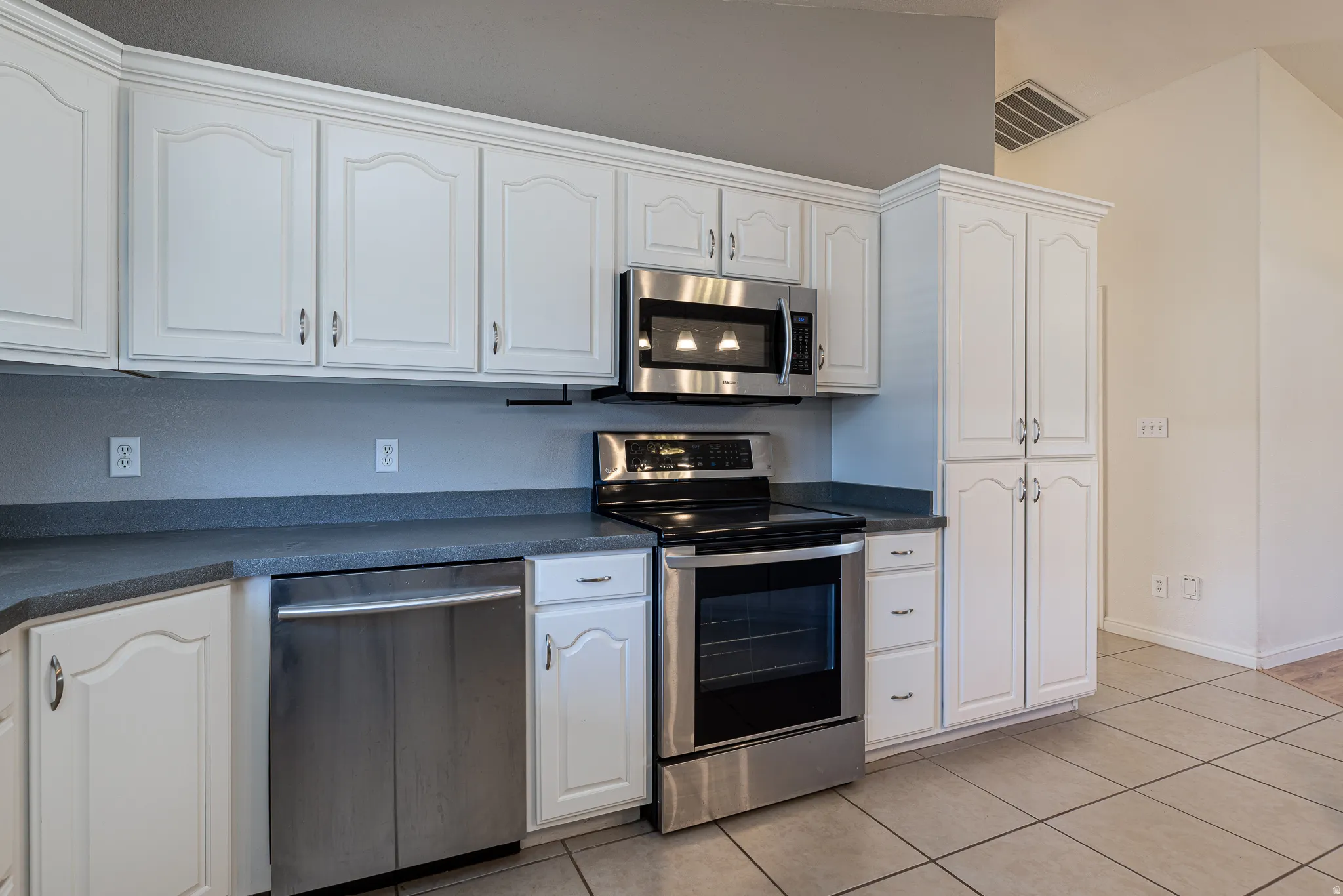 Kitchen with stainless steel appliances, dark countertops, white cabinets, and light tile patterned floors