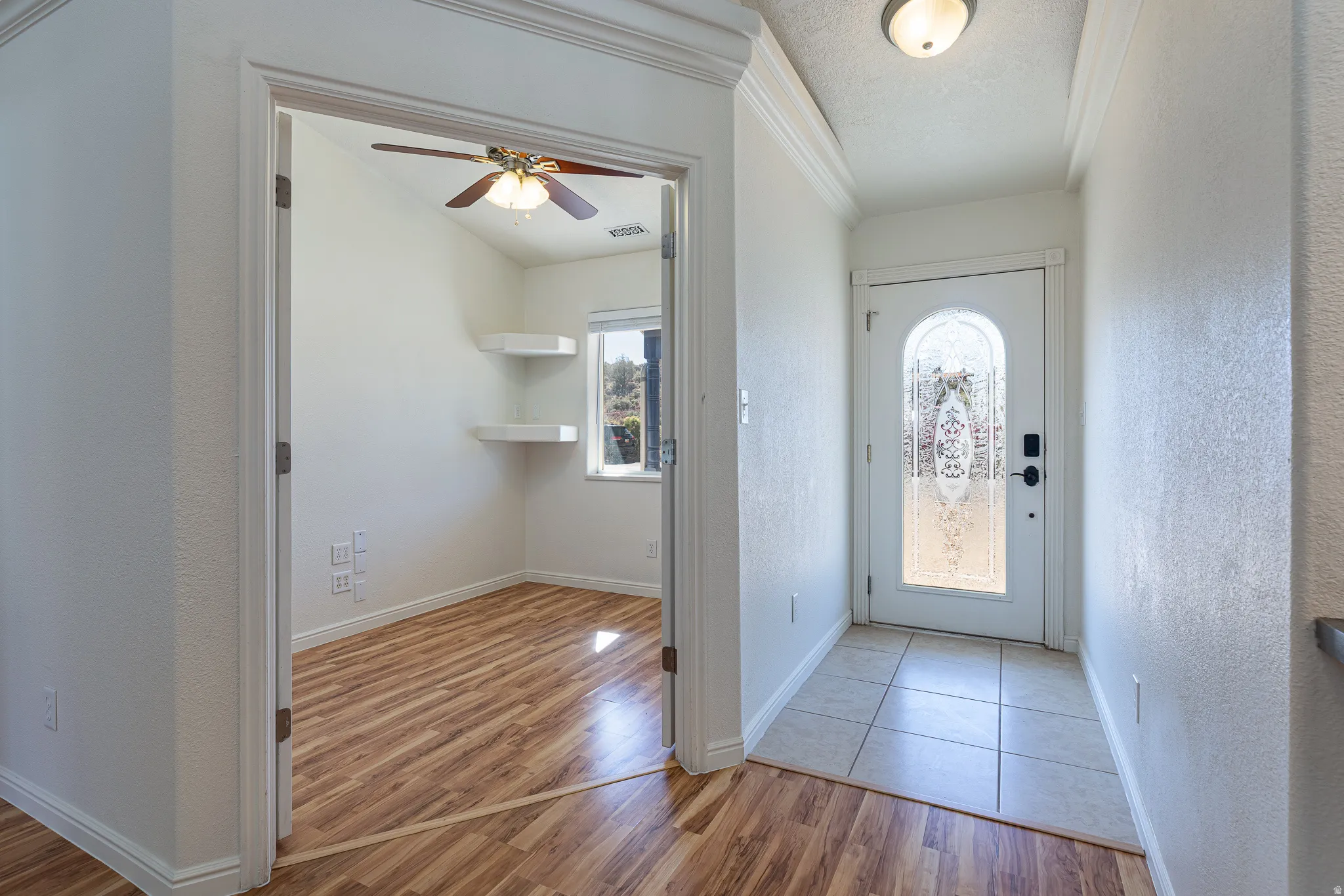 Entrance foyer with ceiling fan, light wood-style floors, a textured ceiling, a textured wall, and ornamental molding