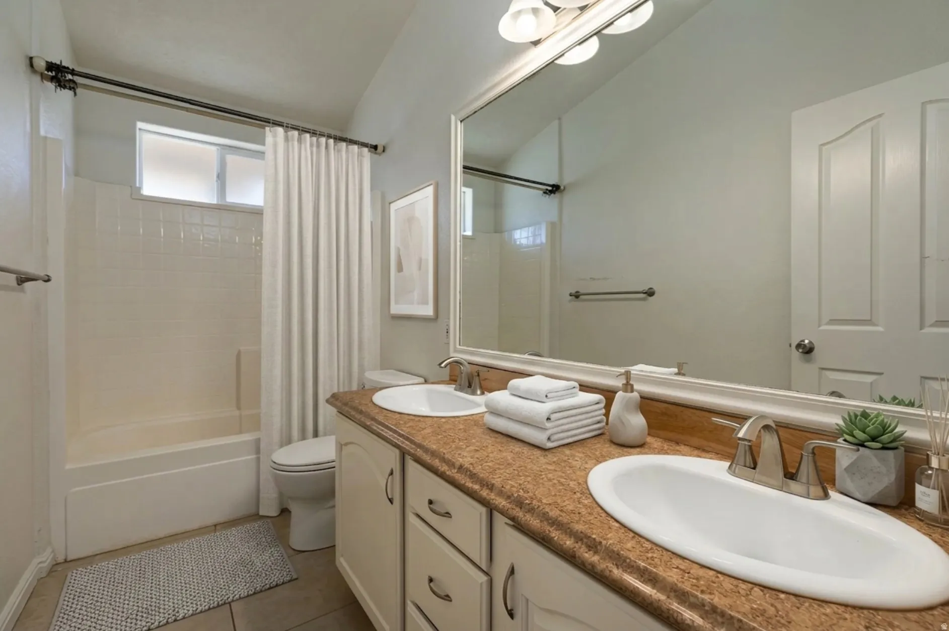 Bathroom with double vanity, shower / bathtub combination with curtain, and light tile patterned flooring