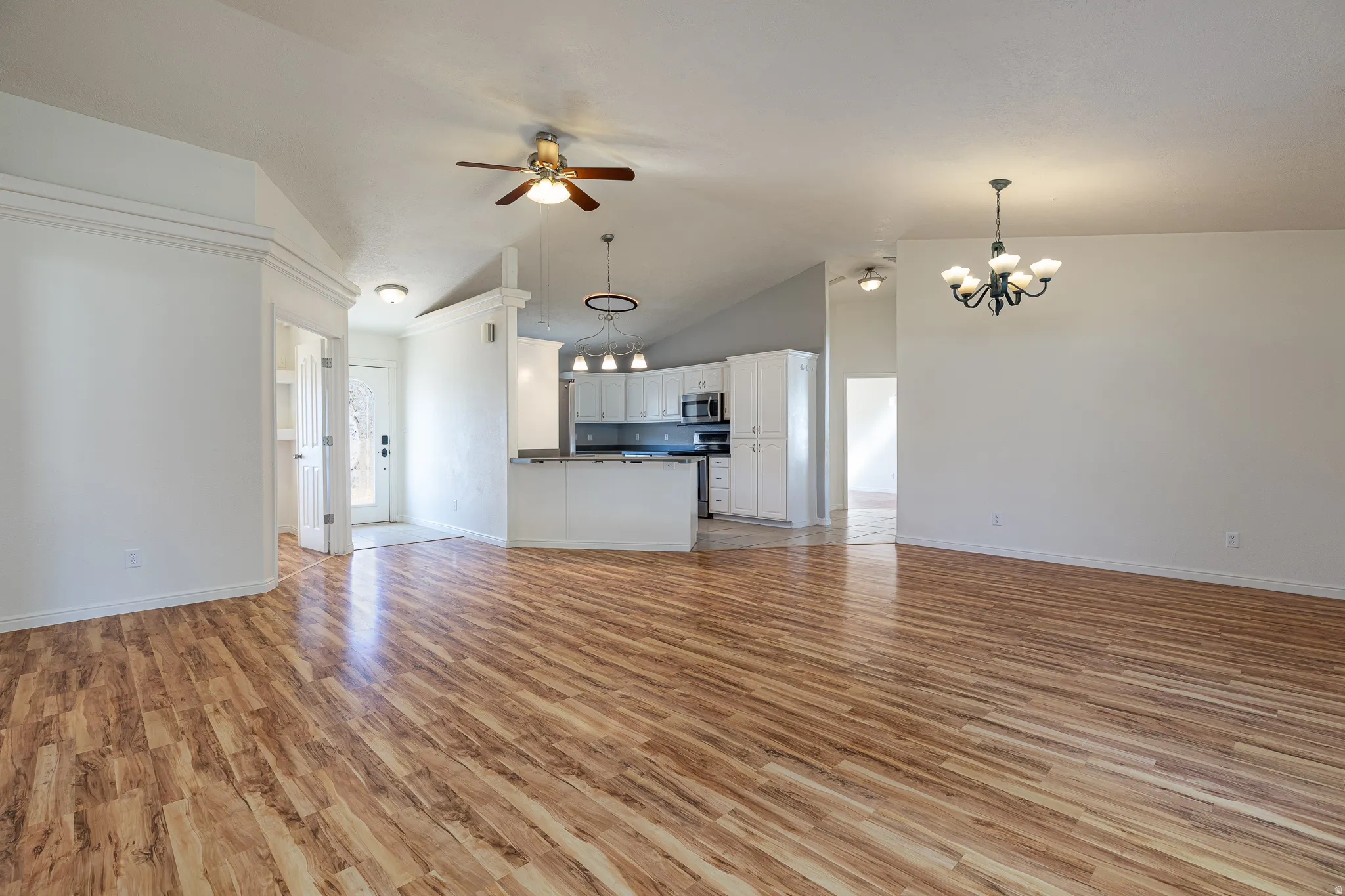 Unfurnished living room featuring suspended lighting, light wood-style flooring, a ceiling fan, and a high ceiling