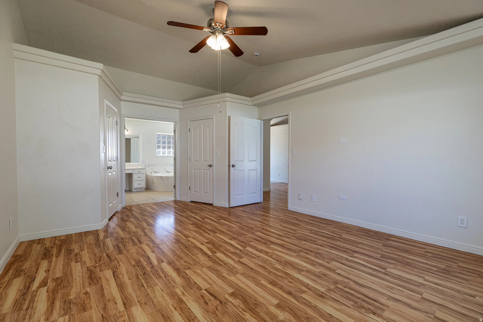 Unfurnished bedroom featuring light wood-style flooring, a ceiling fan, vaulted ceiling, and ensuite bathroom