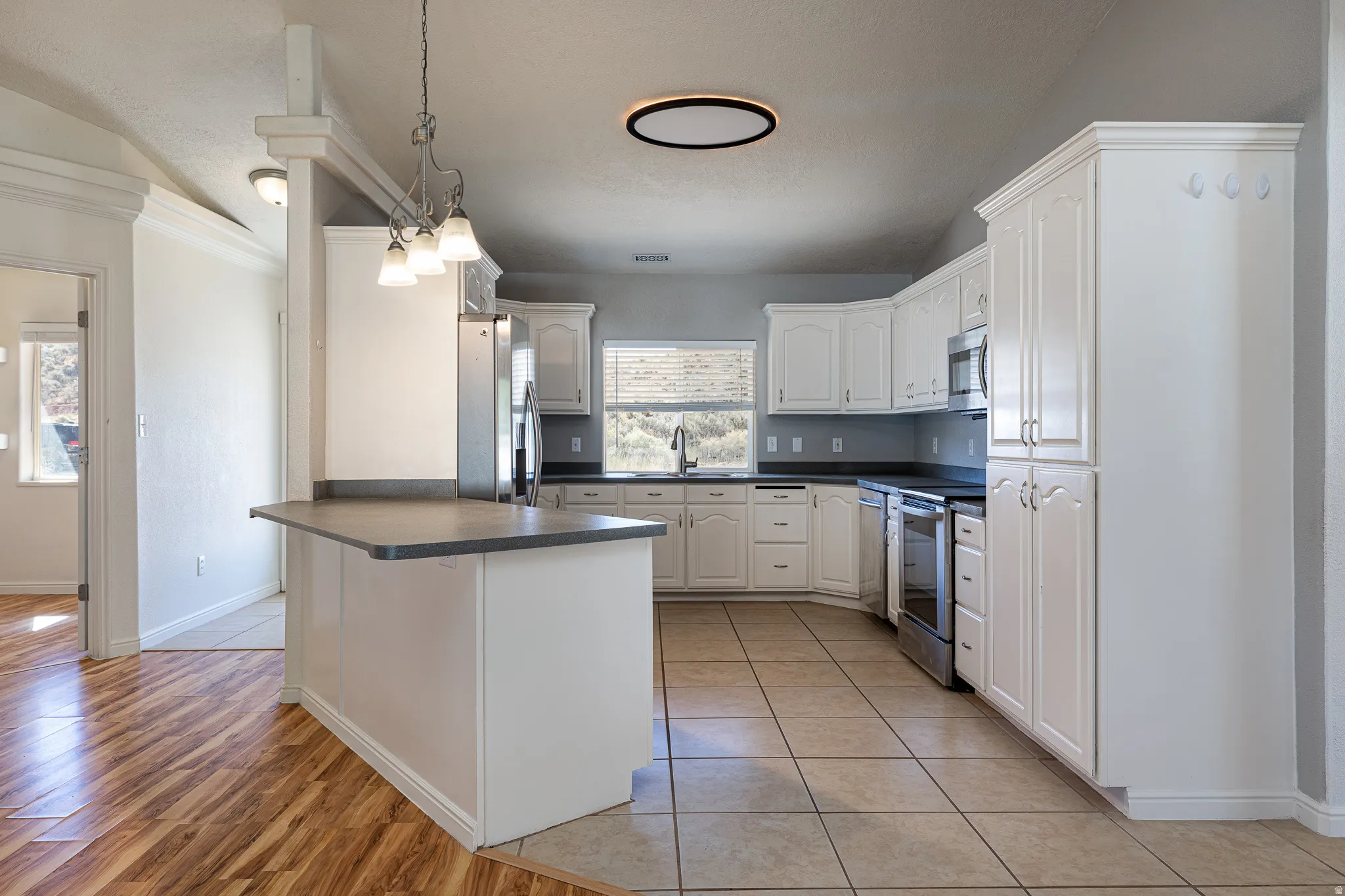 Kitchen with dark countertops, white cabinets, a peninsula, stainless steel appliances, and light tile patterned floors