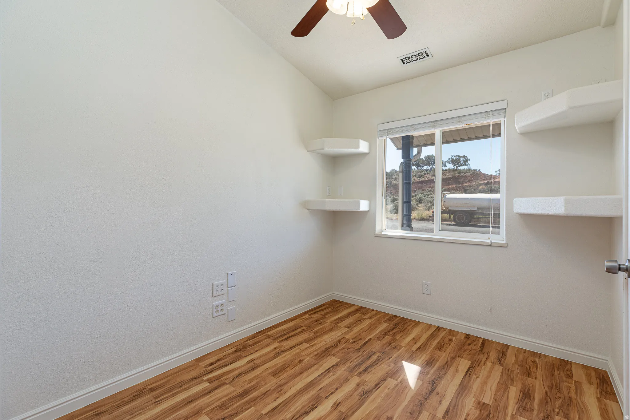 Spare room featuring light wood finished floors, ceiling fan, and lofted ceiling