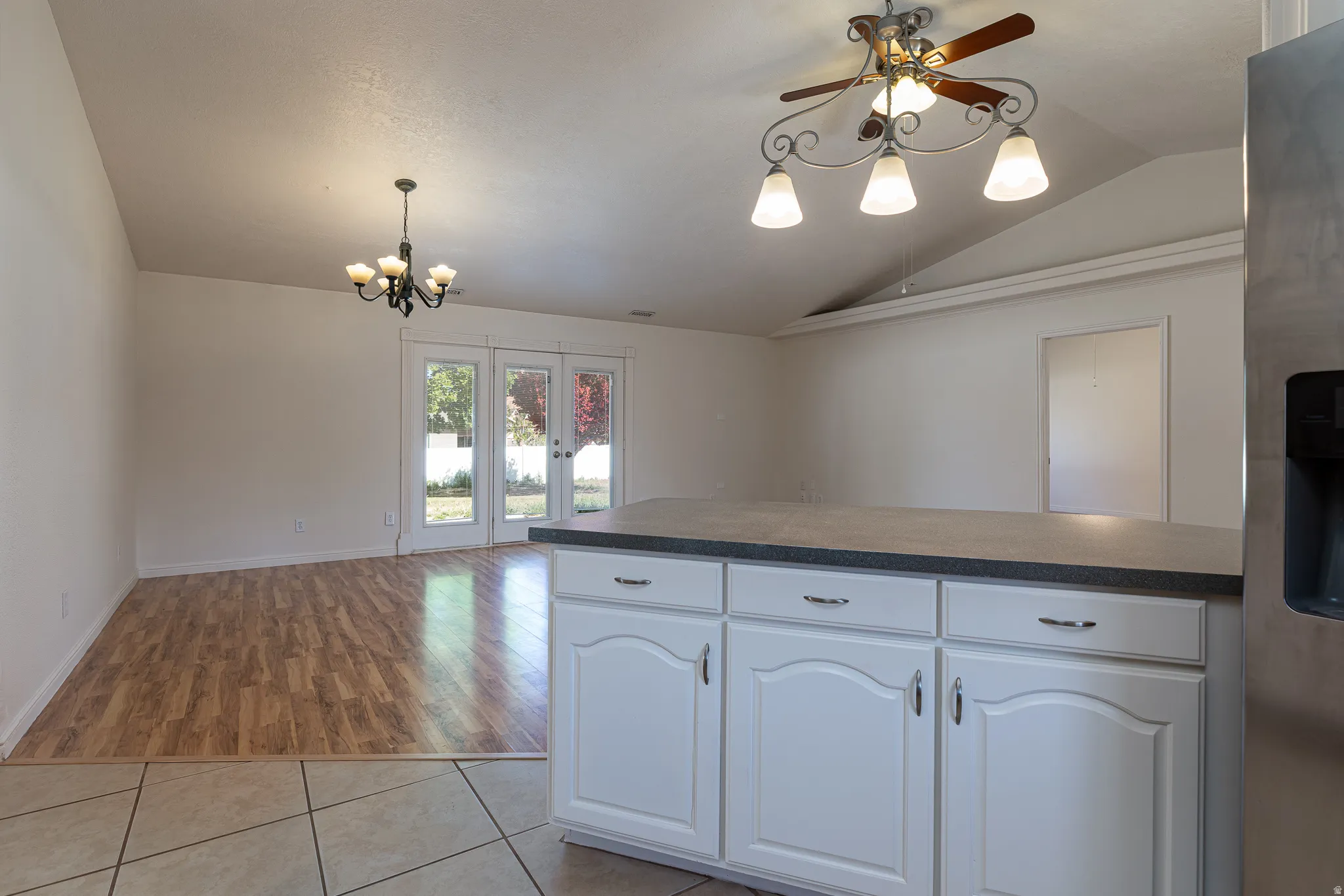 Kitchen with white cabinetry, stainless steel refrigerator with ice dispenser, a ceiling fan, dark countertops, and vaulted ceiling