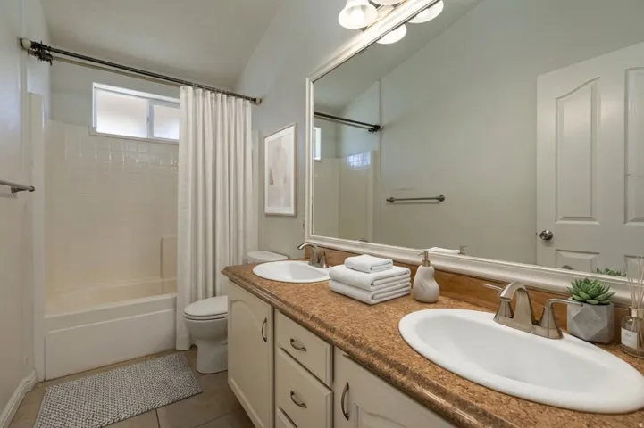 Bathroom with double vanity, shower / bathtub combination with curtain, and light tile patterned flooring