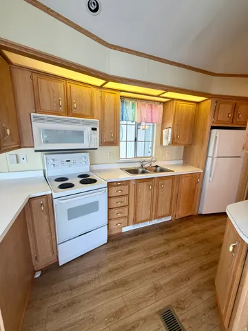 Kitchen with light countertops, white appliances, ornamental molding, light wood finished floors, and wood finish cabinets
